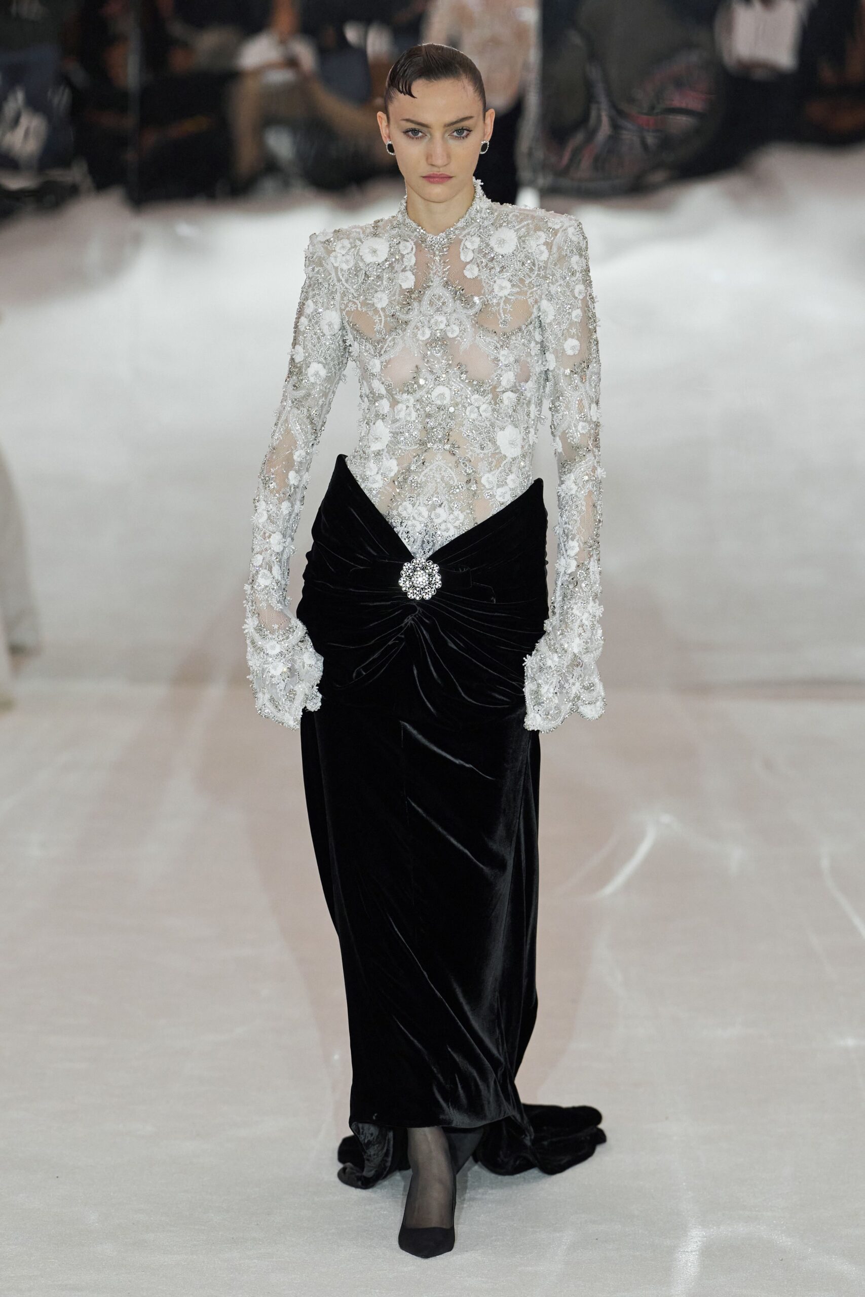 Small silver hoops close to the lobe. Sheer tulle bodice crusted with silver beading and white floral appliqué. Black velvet column skirt, ruched under a crystal cluster at the waist. Sheer black stockings. Black pointed pumps under the hem. For crossing a hotel ballroom after midnight, carrying one last glass.