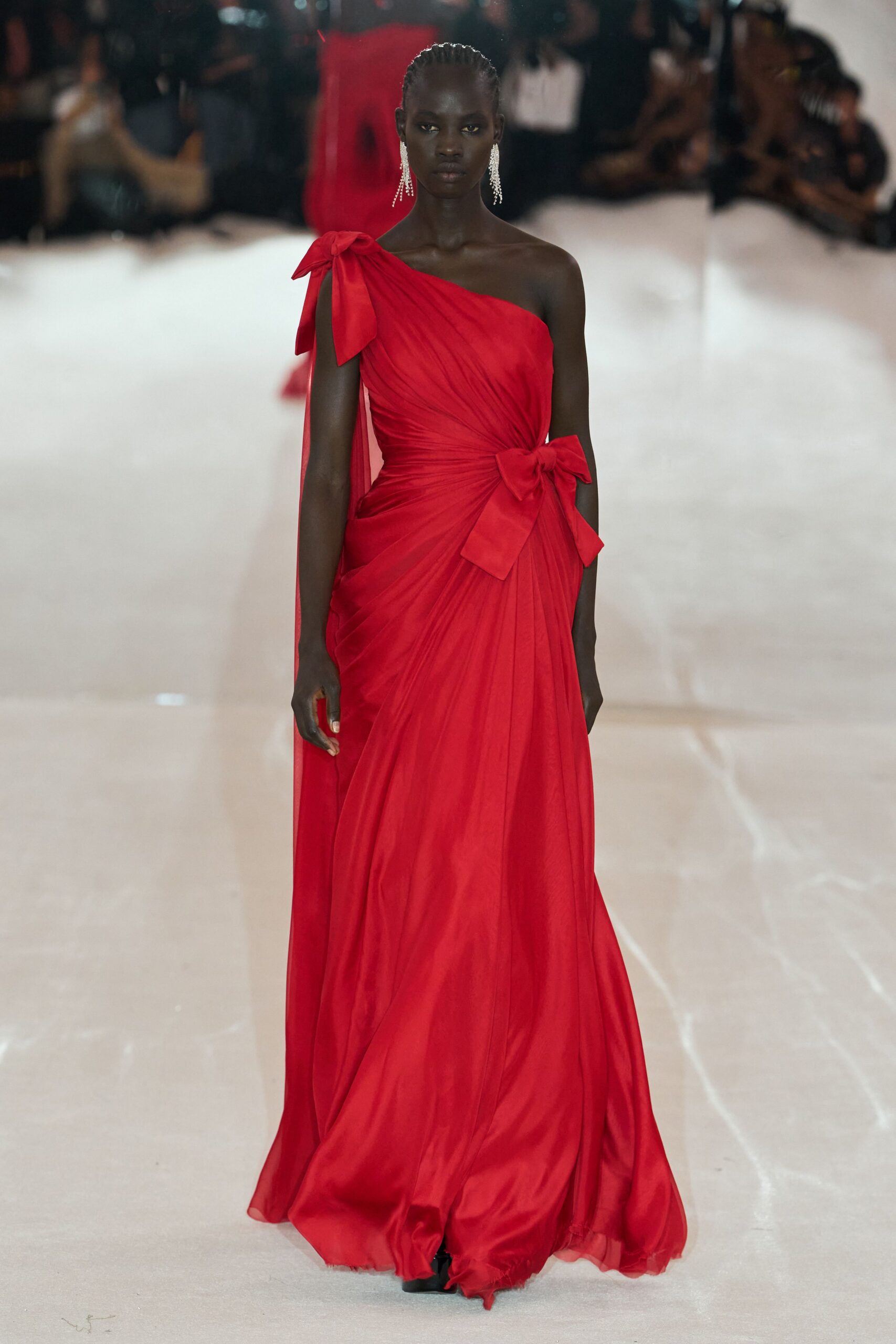 Long crystal fringe earrings brushing the jaw. Scarlet one-shoulder chiffon gown, tightly ruched and knotted with two oversized bows. Crossing a hotel ballroom after the string quartet has packed up.