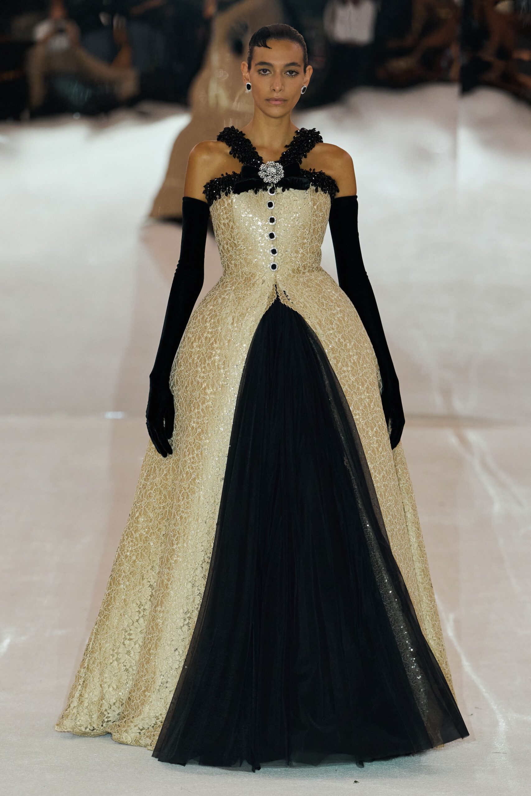 Black cabochon earrings rimmed in silver. Ivory sequined lace ballgown, black tulle inset and jeweled buttons down the front. Opera-length black velvet gloves slipping off the shoulder line. For entering a chandeliered staircase after everyone else has already looked up.