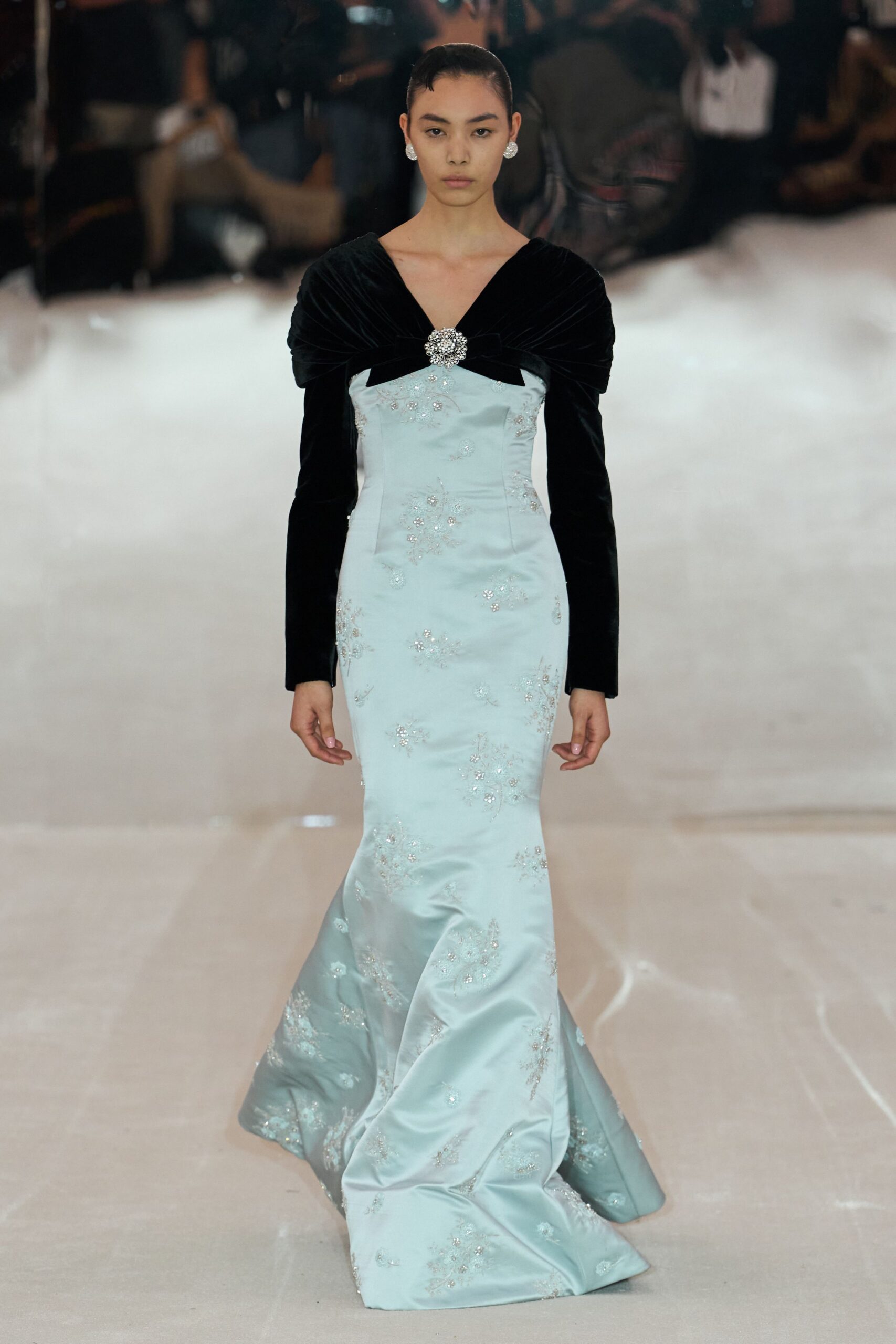 Round crystal cluster earrings. Ice-blue satin column gown with scattered beadwork and a pooling hem. Black velvet bolero draped off the shoulders, pinned with a jeweled brooch. Crossing a hotel ballroom after the orchestra has packed away.