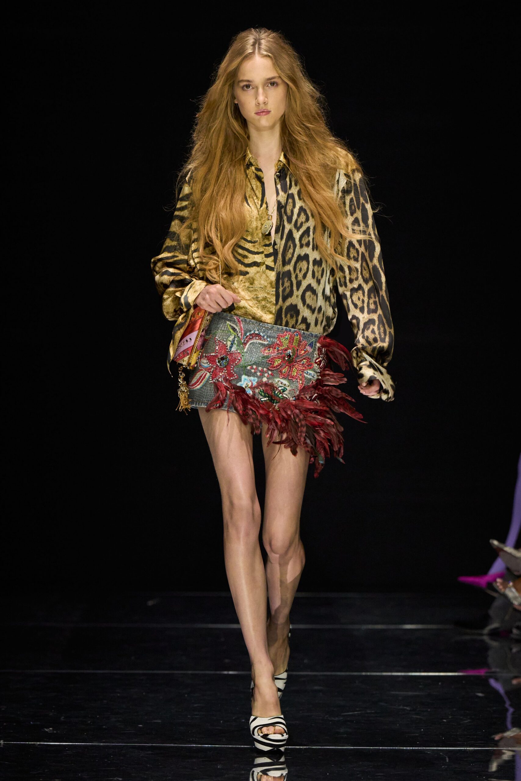 Gold satin blouse split between tiger stripes and leopard spots. Long chain with a teardrop medallion sinking into the placket. Grey reptile-textured mini crusted with sequined flowers and burgundy feathers. Zebra-striped peep-toe heels on a high platform. Walking into a casino bar before sunset, still carrying desert dust.
