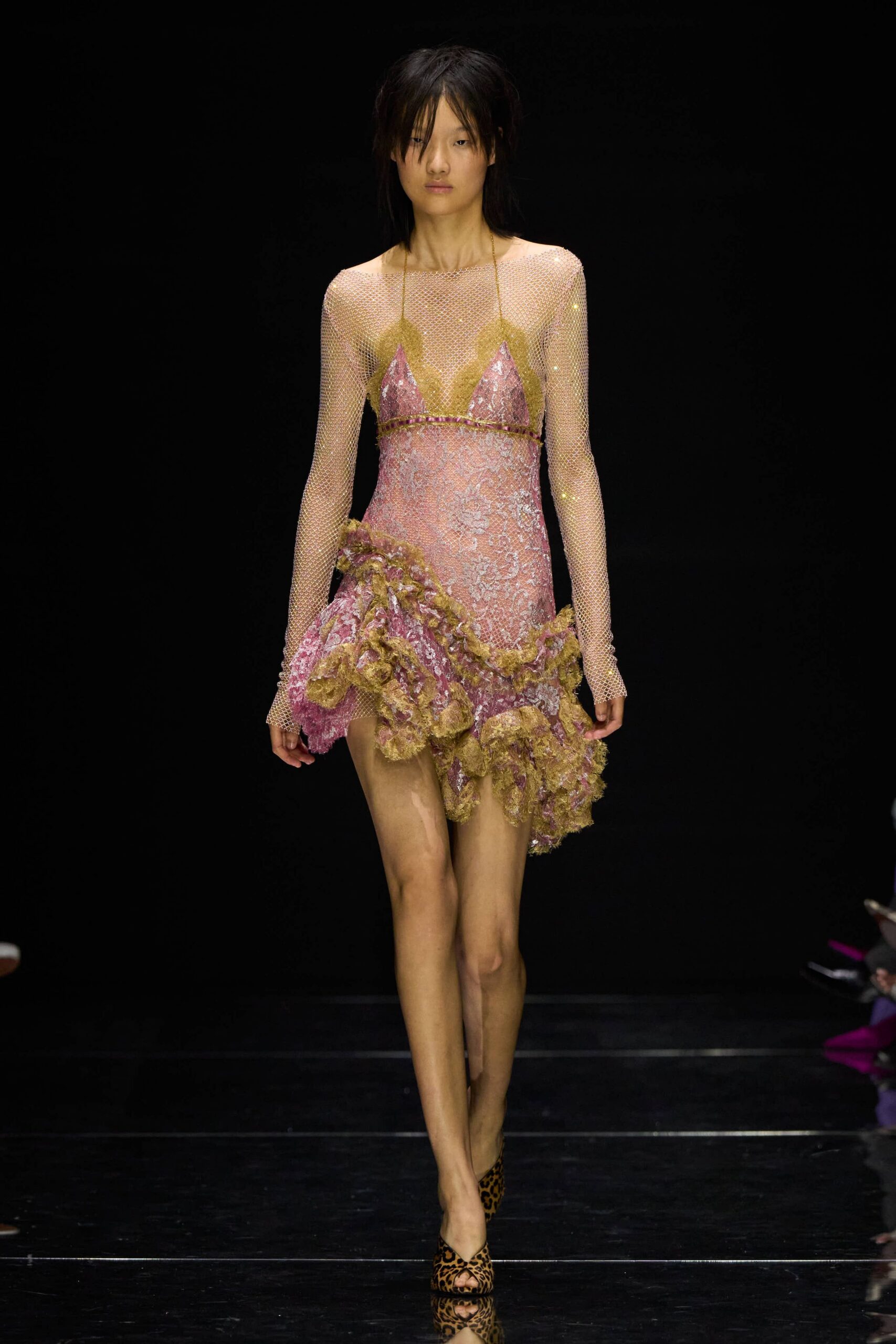Pale gold crystal mesh top, boat neck stretched wide across the shoulders. Pink brocade slip dress with olive lace cups and a beaded underbust seam. Asymmetric hip ruffle in shredded gold lace, kicked outward at one side. Leopard calf-hair peep-toe mules. Walking back from a casino wedding with confetti still in your hair.