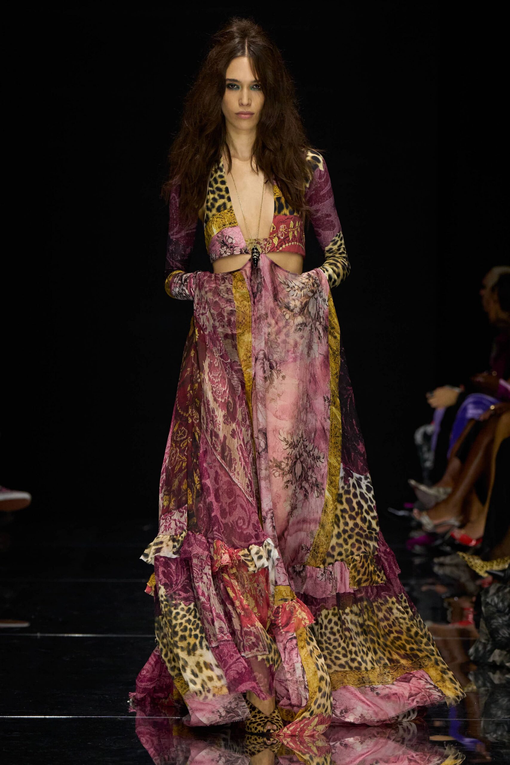 Patchworked mesh gown in mauve, mustard and leopard, cut to the navel. Long pendant dropping into the ringed front cutout. Leopard sandals peeking under the pooled ruffle hem. Walking back from a beach wedding after the music has thinned out.