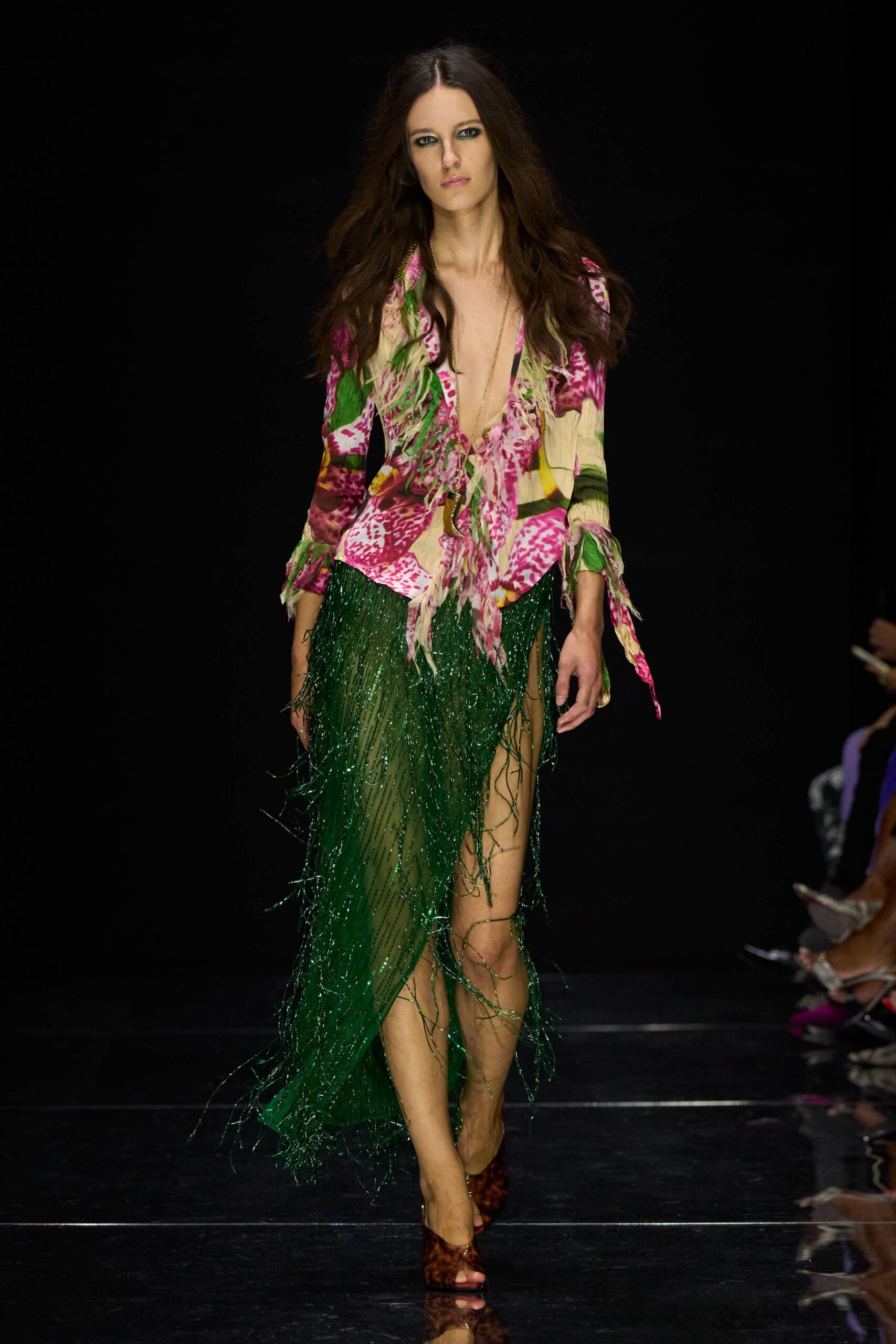 Plunging floral blouse in crinkled chiffon, ruffled ties hanging loose at the cuffs. Long chain pendant dropping into the open neckline. Emerald beaded fringe skirt, sheer underlayer flashing through the high split. Tortoiseshell peep-toe heels. Crossing a hotel terrace after midnight, still damp from the pool.