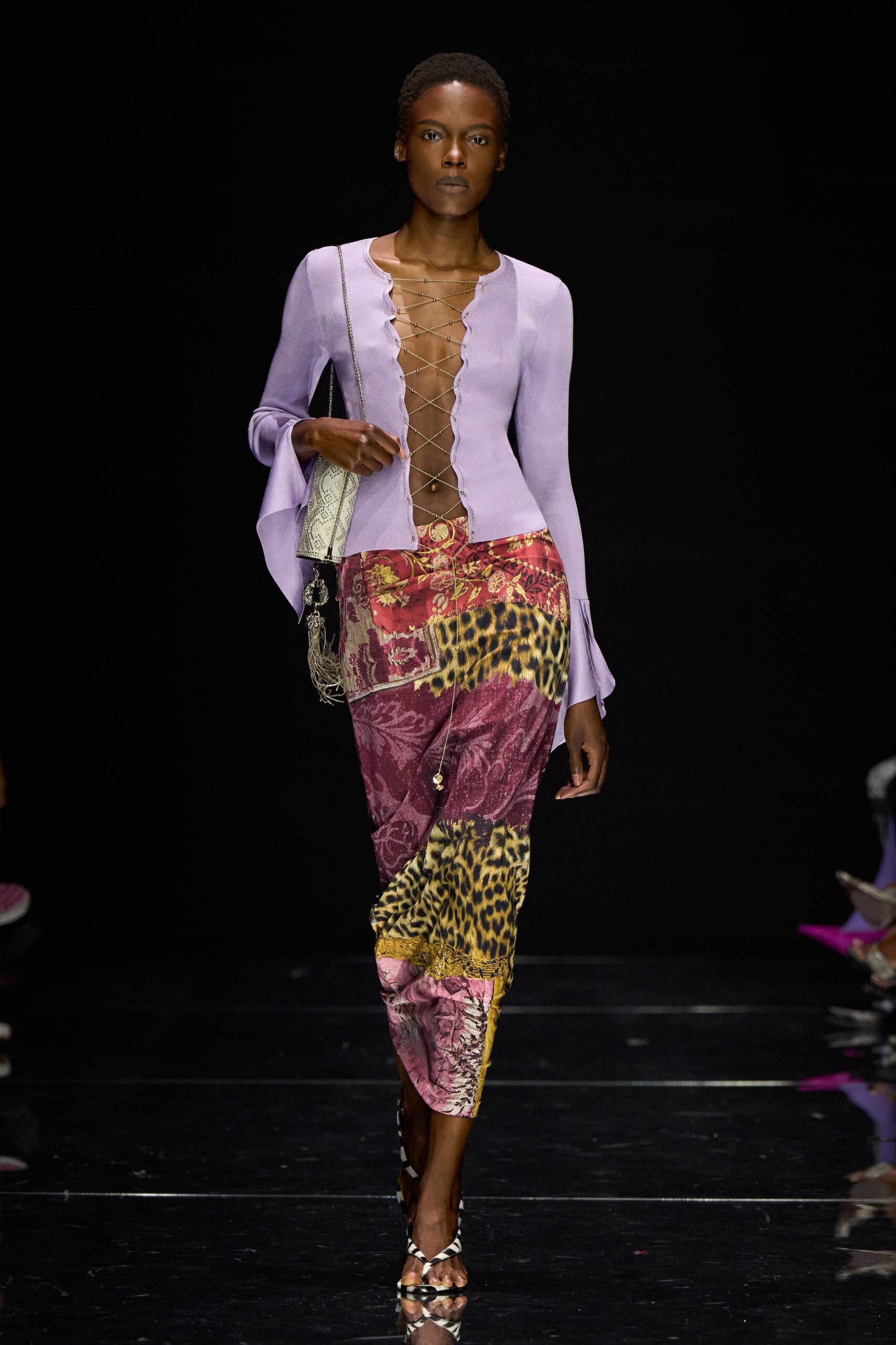 Lilac ribbed cardigan, split cuffs and a deep chain-laced opening. Pale python shoulder bag with a silver tassel charm. Bias-cut patchwork skirt mixing leopard panels with wine brocade. Zebra-print thong sandals. For picking up warm fruit from a street stall after midnight.