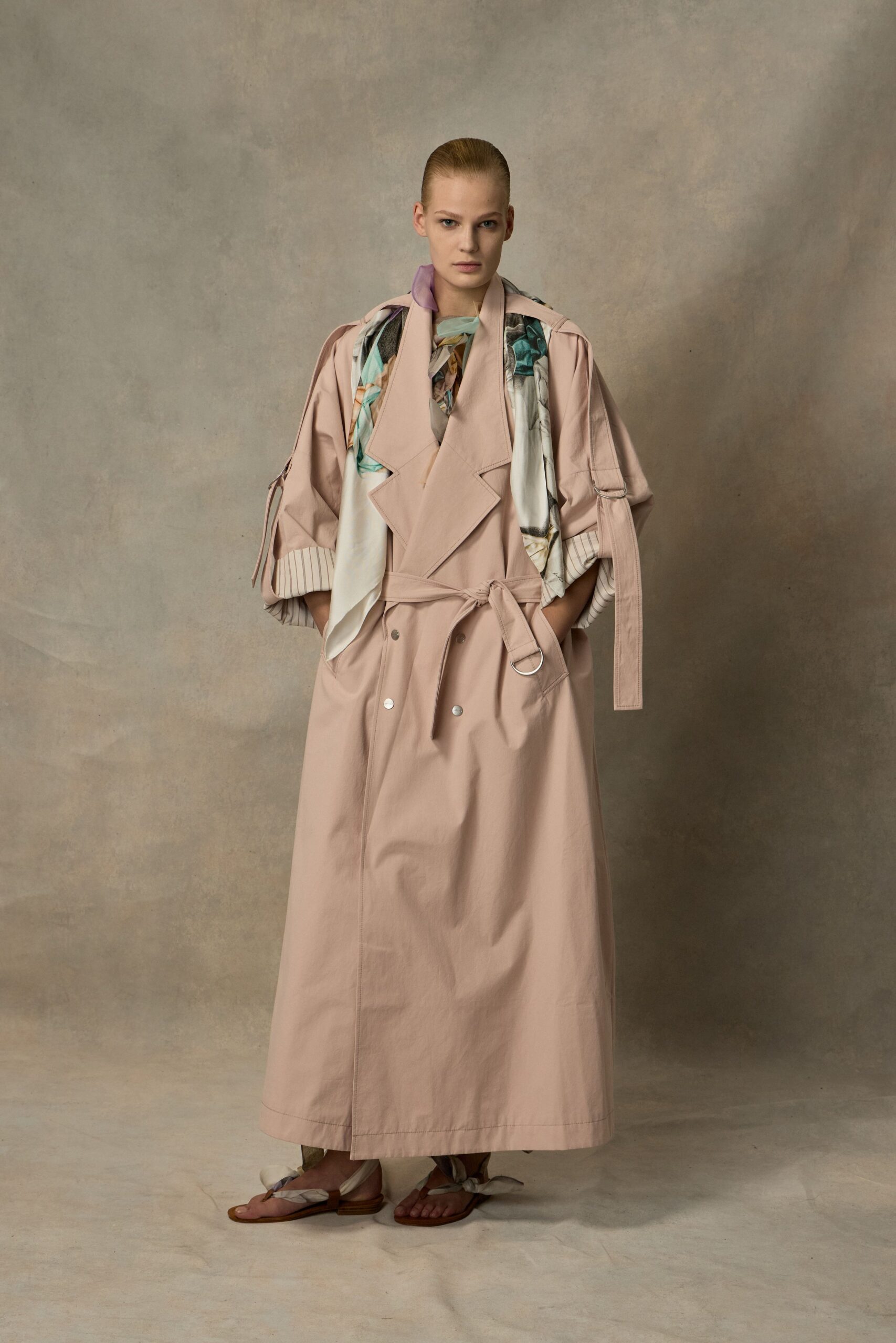 Blush cotton trench, cut full and long with silver snaps. Painterly silk scarf draped through the open lapels. Flat sandals tied with twisted fabric at the toes. For walking the hotel garden before breakfast while the sprinklers still tick.