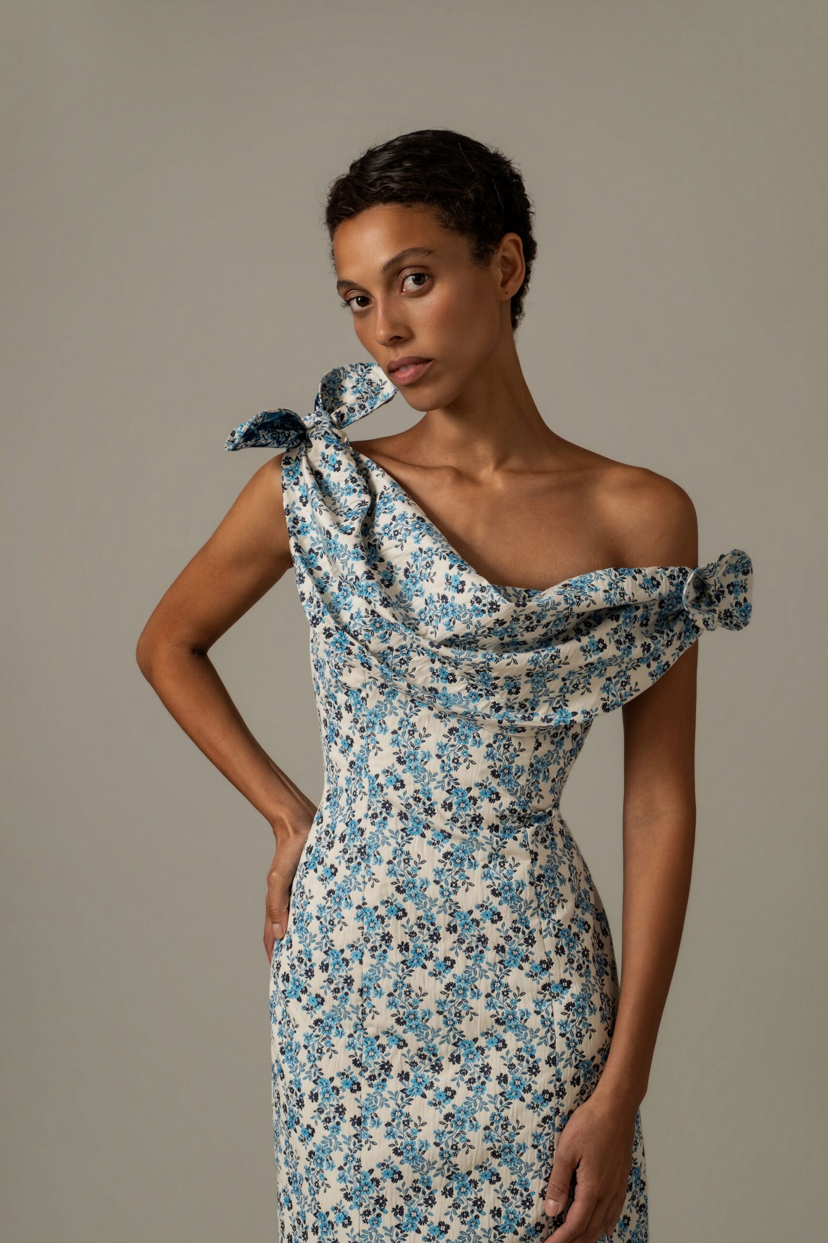 Ivory floral dress in lightly crinkled fabric, draped off-shoulder neckline tied into side bows. Garden wedding after the chairs have been folded and stacked.