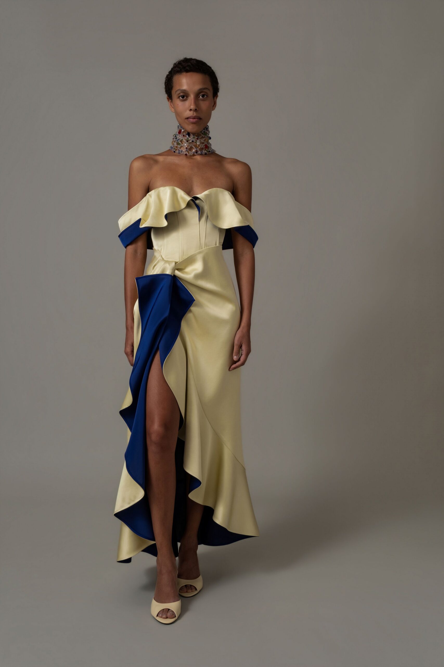 Clear crystal mesh choker pricked with multicolored stones. Butter-cream satin gown with corseted seams and cobalt-backed ruffles. Cream peep-toe mules. For accepting flowers in a museum atrium after the quartet stops.