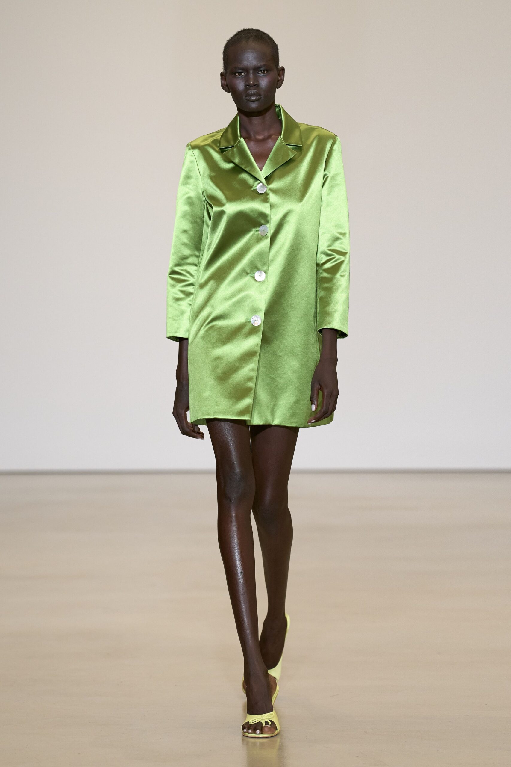 Acid-lime satin coatdress, cut straight with four pearly buttons. Pale chartreuse thong mules with a tiny bow at the toe. Hotel corridor at noon, carrying room-service coffee back one-handed.