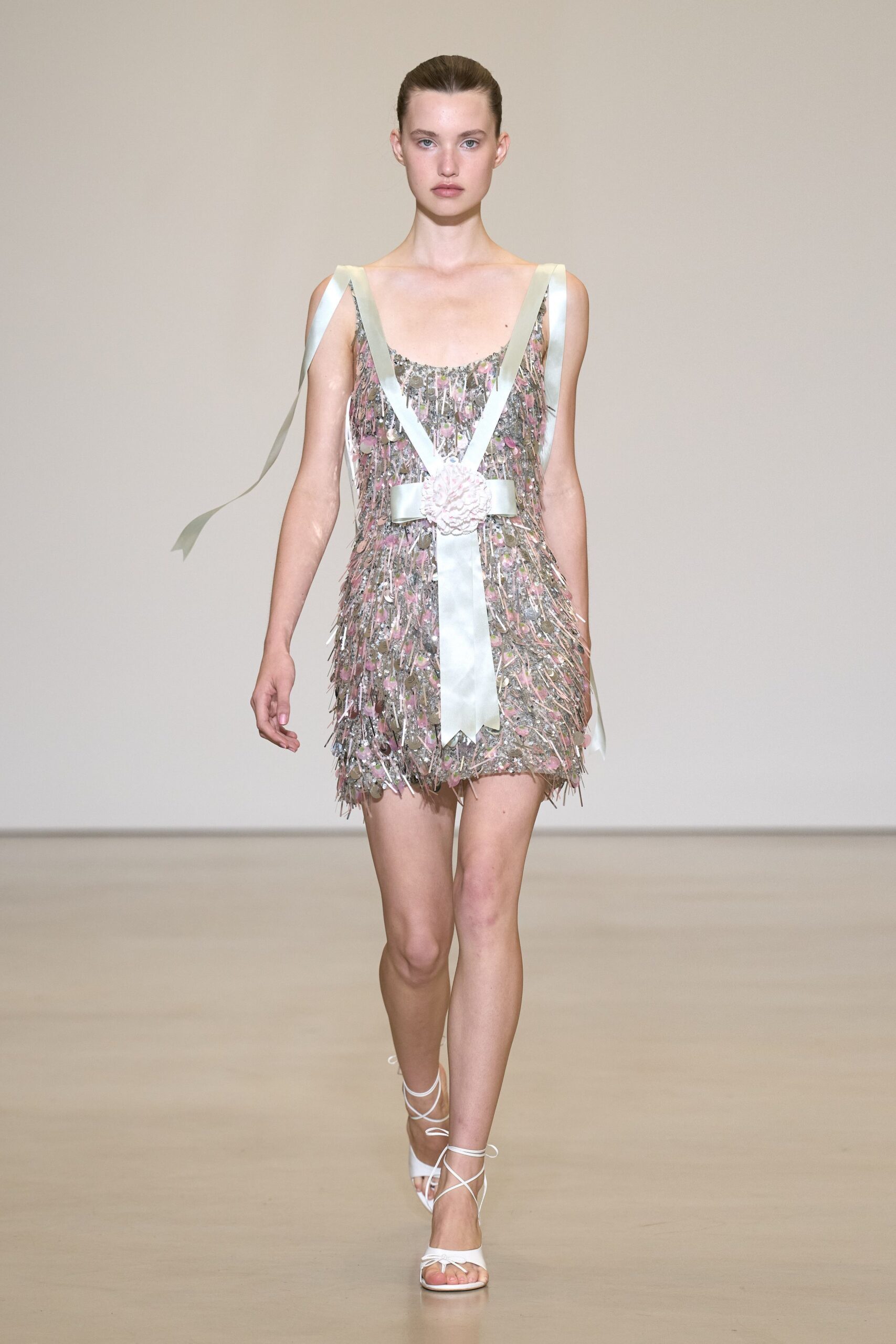 Silver sequin slip mini shagged with pink paillettes and tinsel fringe. Wide ivory satin ribbons crossed low, pinned with a crumpled rosette. White lace-up sandals with thin cords winding the ankle. Walking out of a hotel ballroom after the flower girls found the confetti cannon.