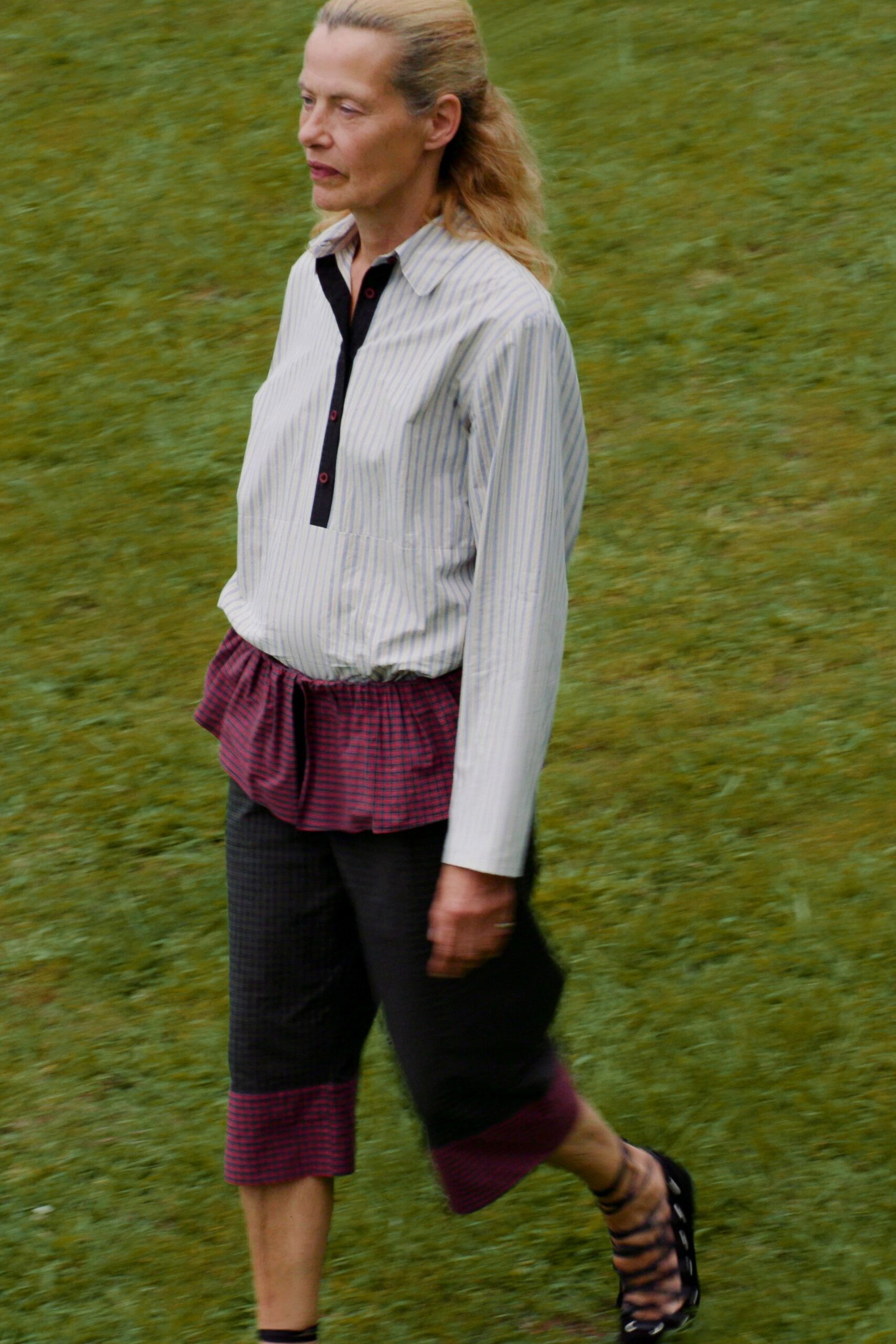 Pale blue banker stripes with a black half placket and red buttonholes. Black microcheck cropped trousers with raspberry gingham ruffles at waist and cuff. Black lace-up heels with sheer smoky striped panels. Crossing wet grass after lunch at a country hotel nobody dressed for.