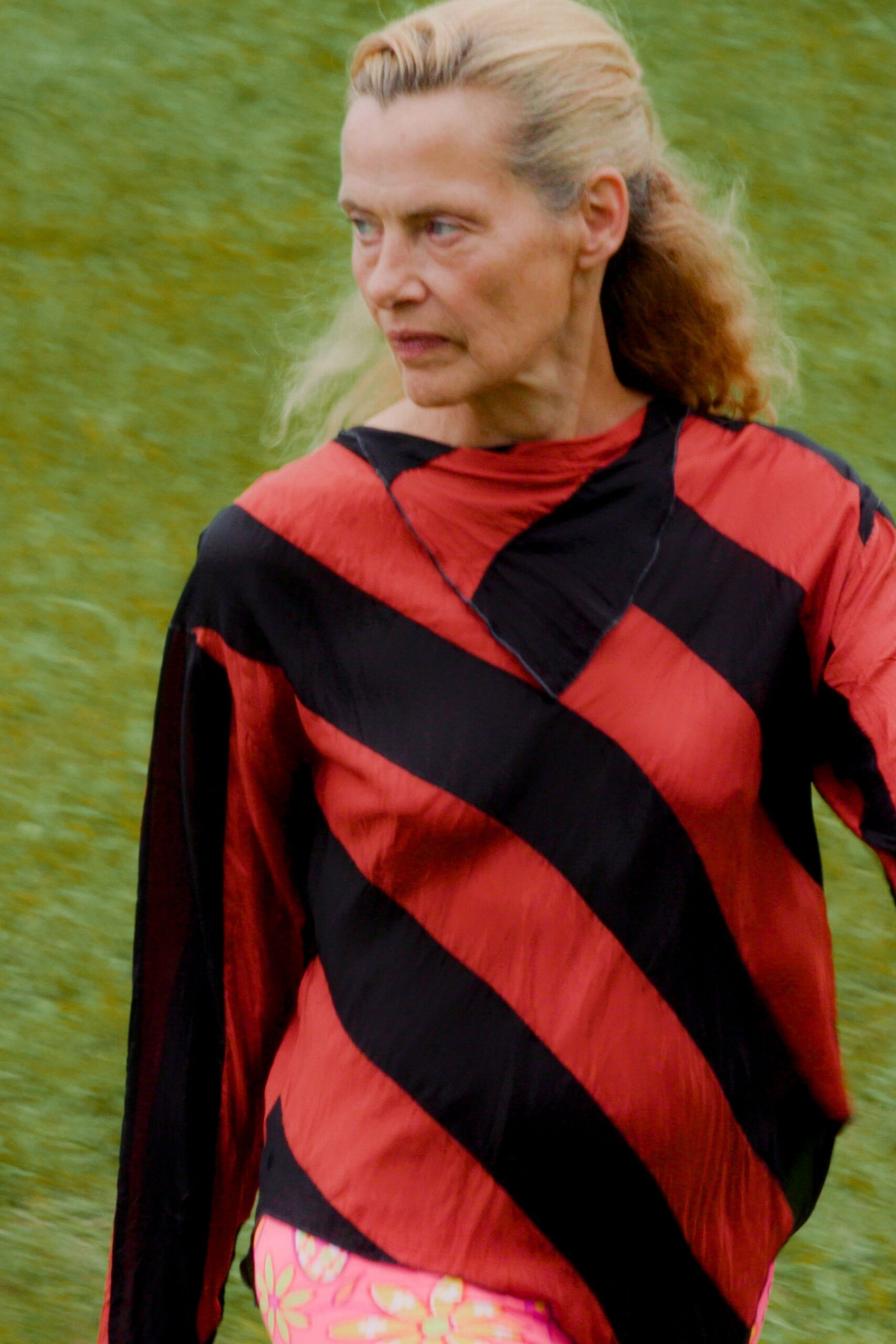 Tomato-red crinkled top banded with broad black diagonal stripes. Hot-pink floral skirt peeking out at the hemline. Crossing wet grass after the fair, still in yesterday's makeup.