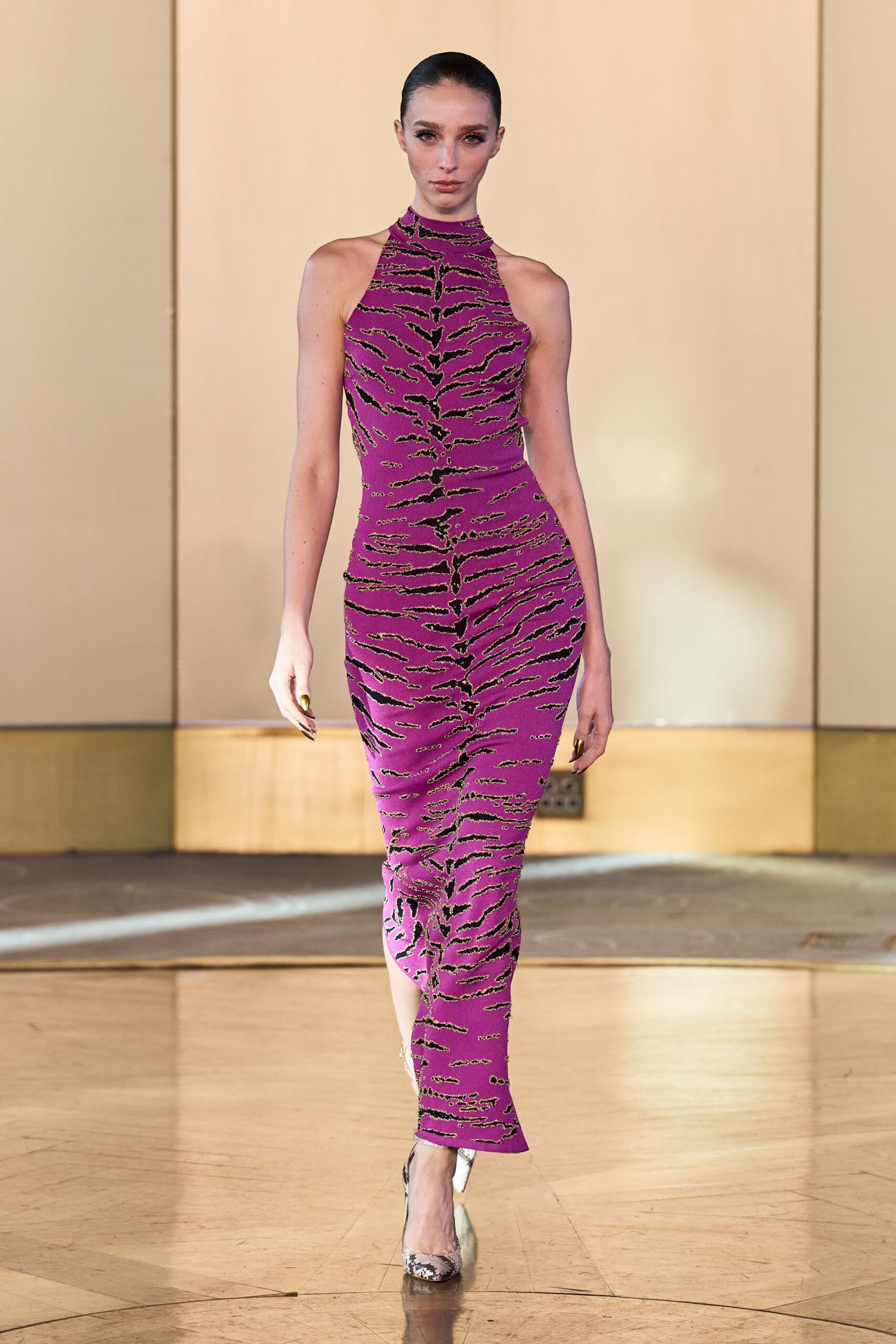 Fuchsia column dress in glittering tiger-stripe knit, cut with a close halter neck. Pointed python pumps flashing silver at the sides. Hotel ballroom carpet just beyond the doors, somebody else's wedding downstairs.