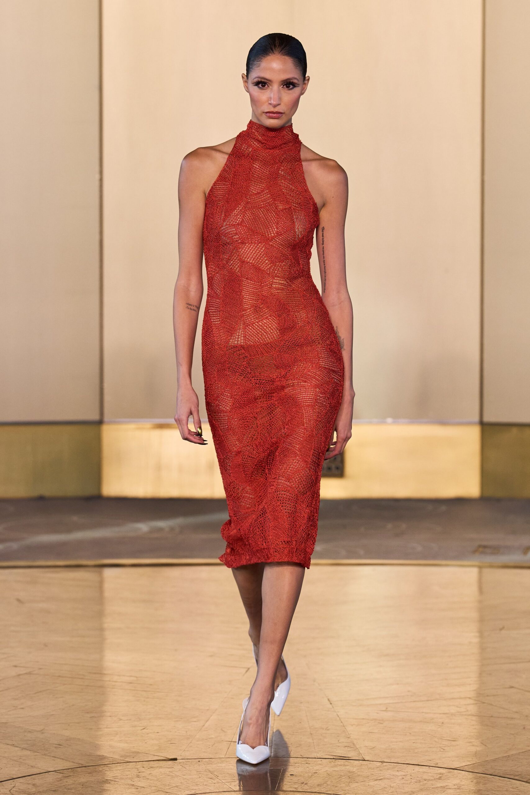 Rust open-knit halter dress, geometric stitches turning sheer across the torso. White patent pumps with a sharp dipped vamp. Waiting for the restaurant patio heater to catch after sunset.
