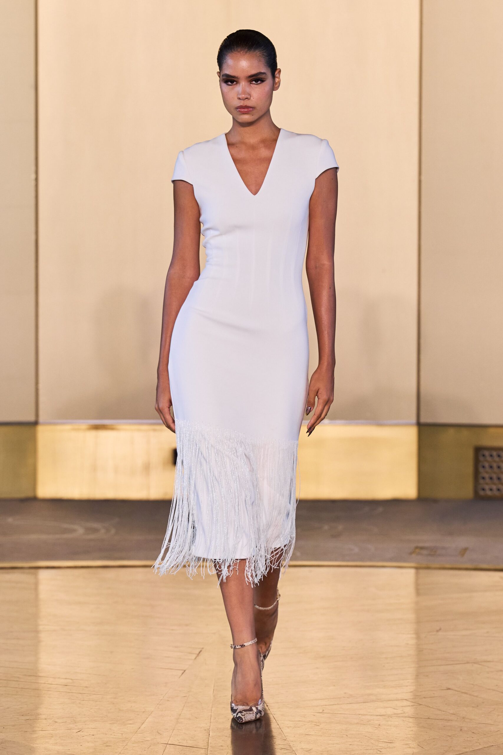 Pale fitted crepe dress with cap sleeves and a low V neck. Long white fringe swaying from a dropped handkerchief panel. Python pointed pumps with a thin silver ankle strap. For arriving at a hotel wedding after the speeches already started.