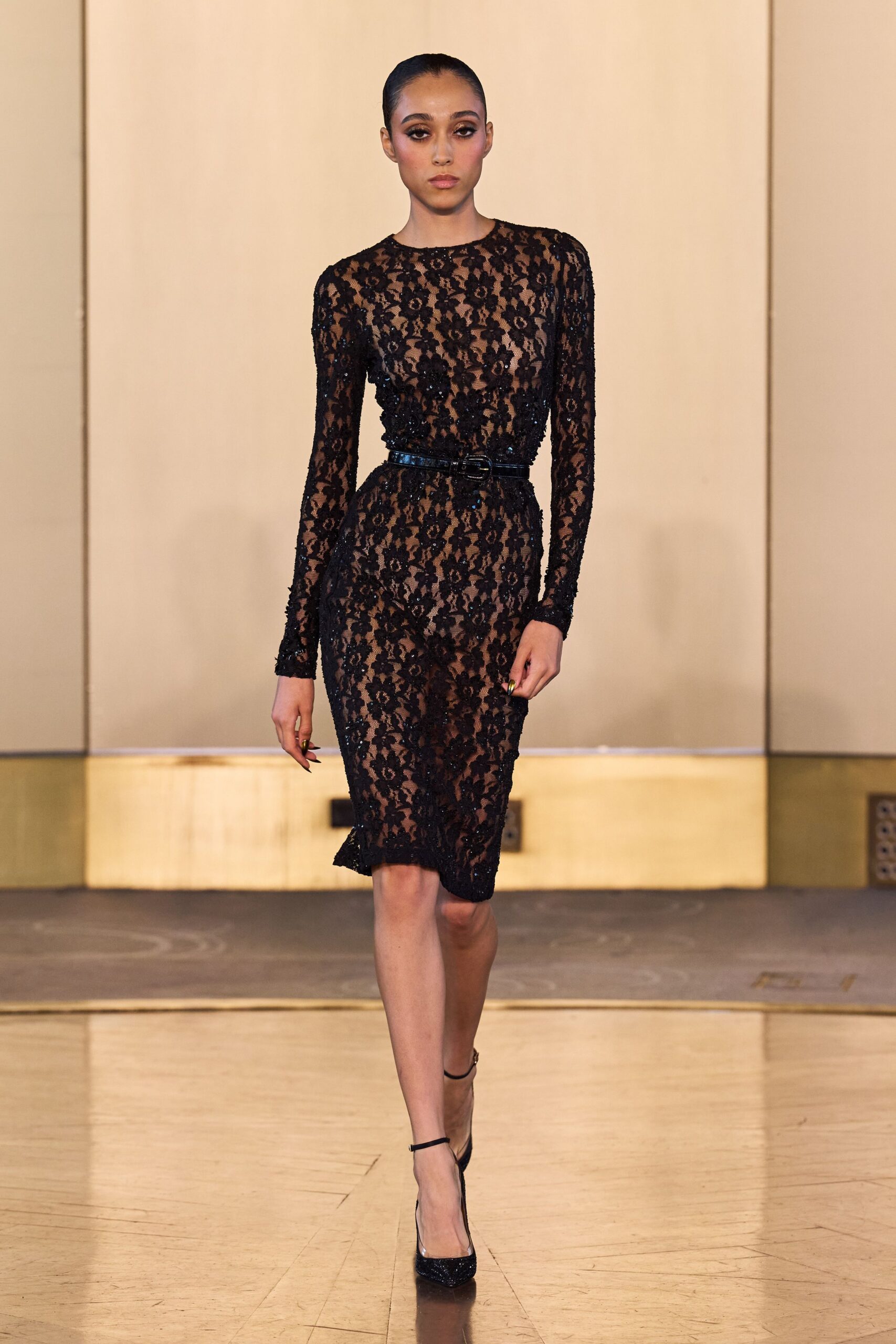 Sheer black floral lace dress over nude lining, long sleeves and pencil hem. Patent black belt cinching the waist with a small oval buckle. Black ankle-strap pumps with glitter packed across the pointed toe. Walking into a hotel bar before anyone has put their coat down.