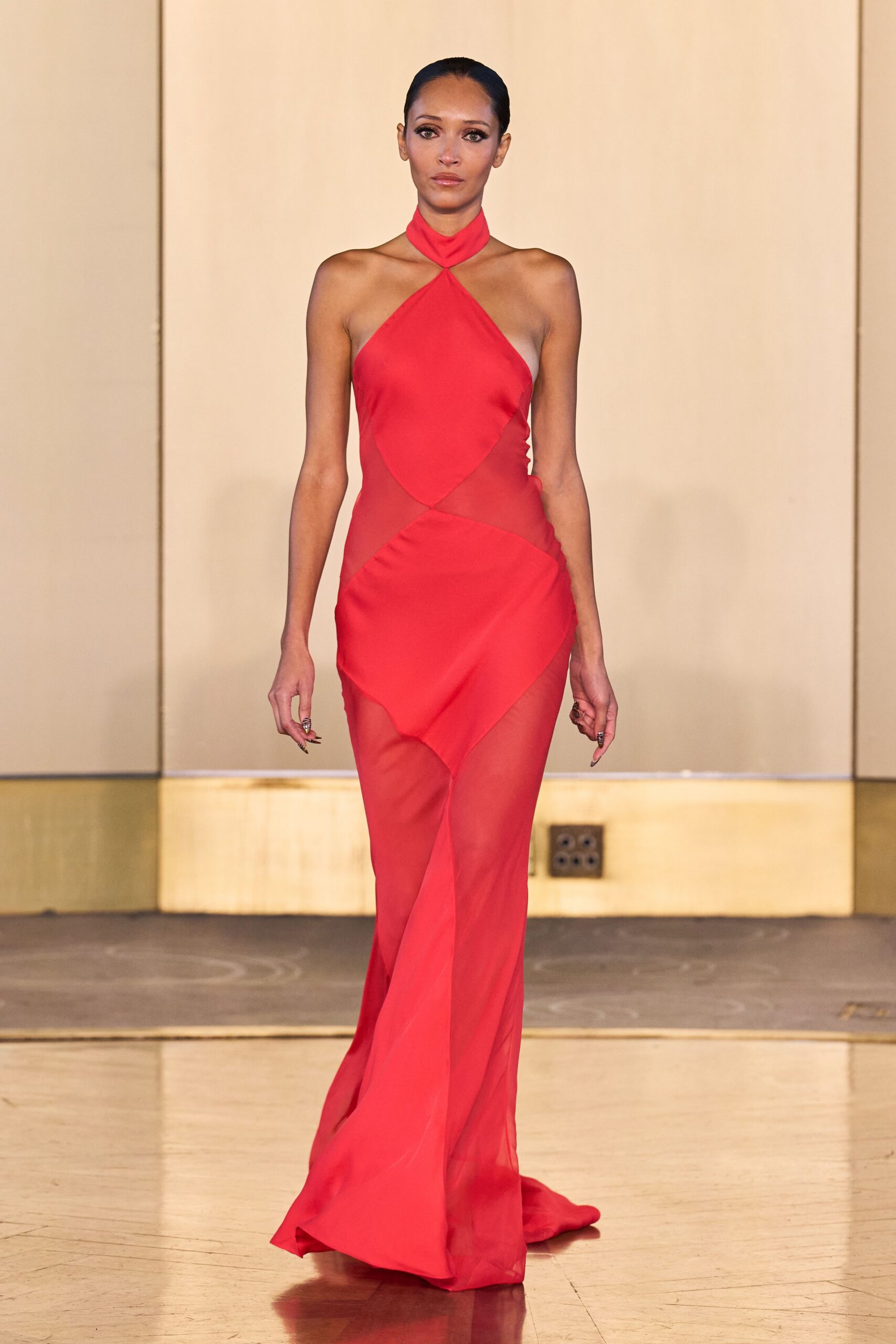 Scarlet halter gown with sheer mesh cutouts and a twisted choker neckline. After midnight at a hotel wedding, crossing the ballroom barefoot in your head.