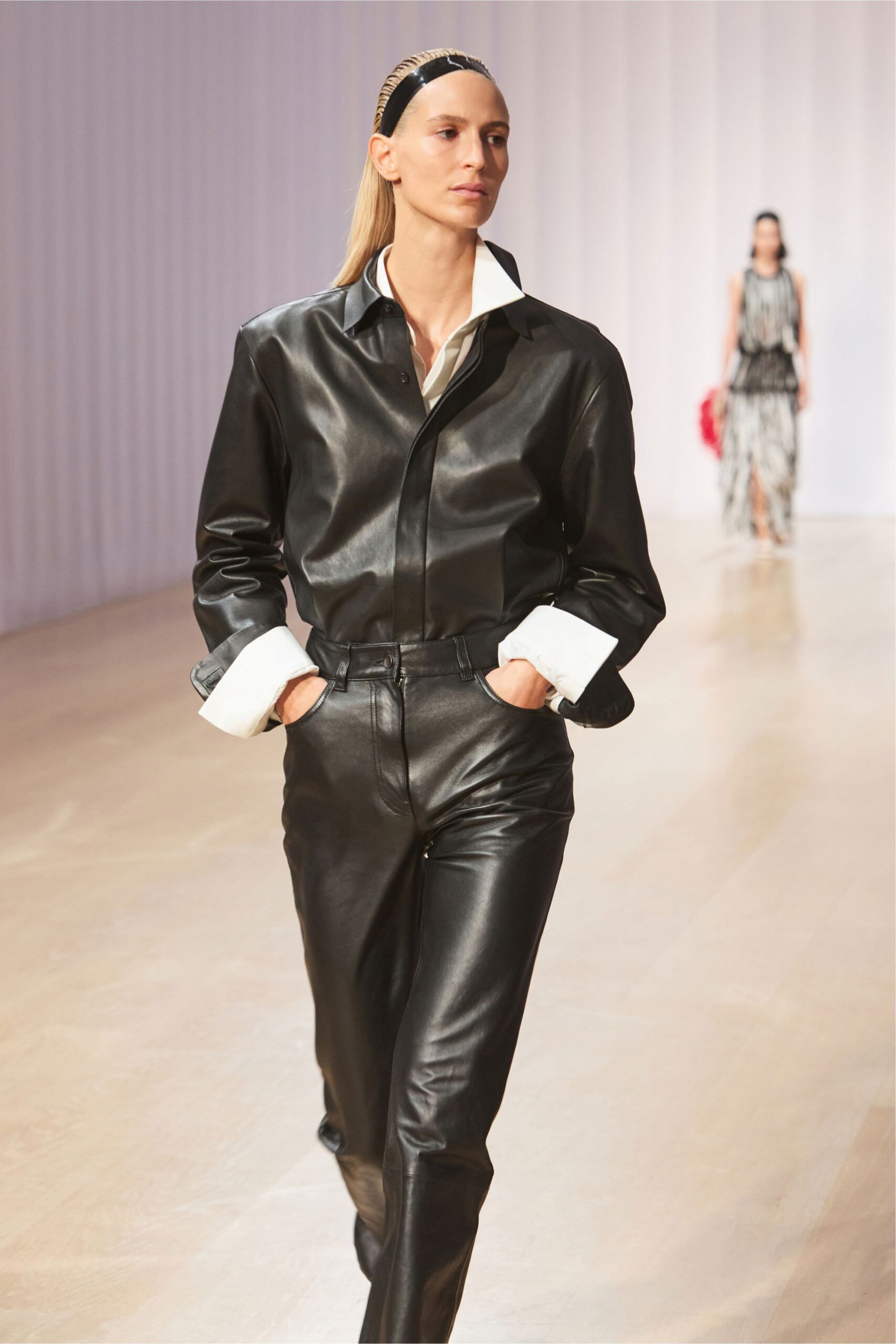 Black patent band with a narrow braided edge. White shirt collar and deep cuffs jutting from black leather. Glossy black leather with a covered placket and soft creases. High-waisted black leather trousers, front pockets cut on a curve. For the school pickup that turns into a lawyer's lunch.