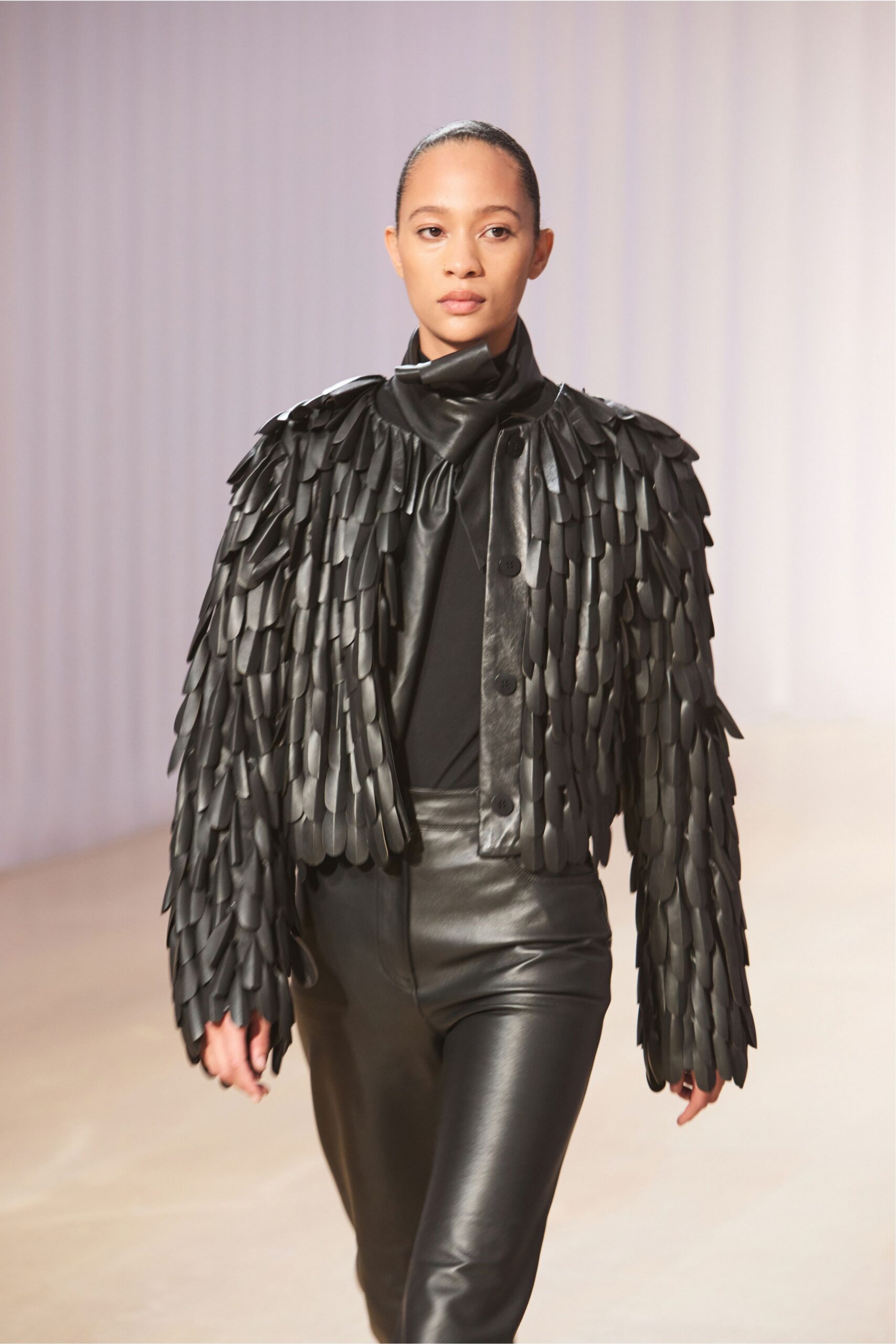 Black leather jacket densely appliqued with overlapping petal scales, one button exposed. Black draped-neck top, the collar folding into a soft twist. High-waisted black leather trousers with a smooth second-skin shine. Whatever you wear home after the museum benefit runs past midnight.
