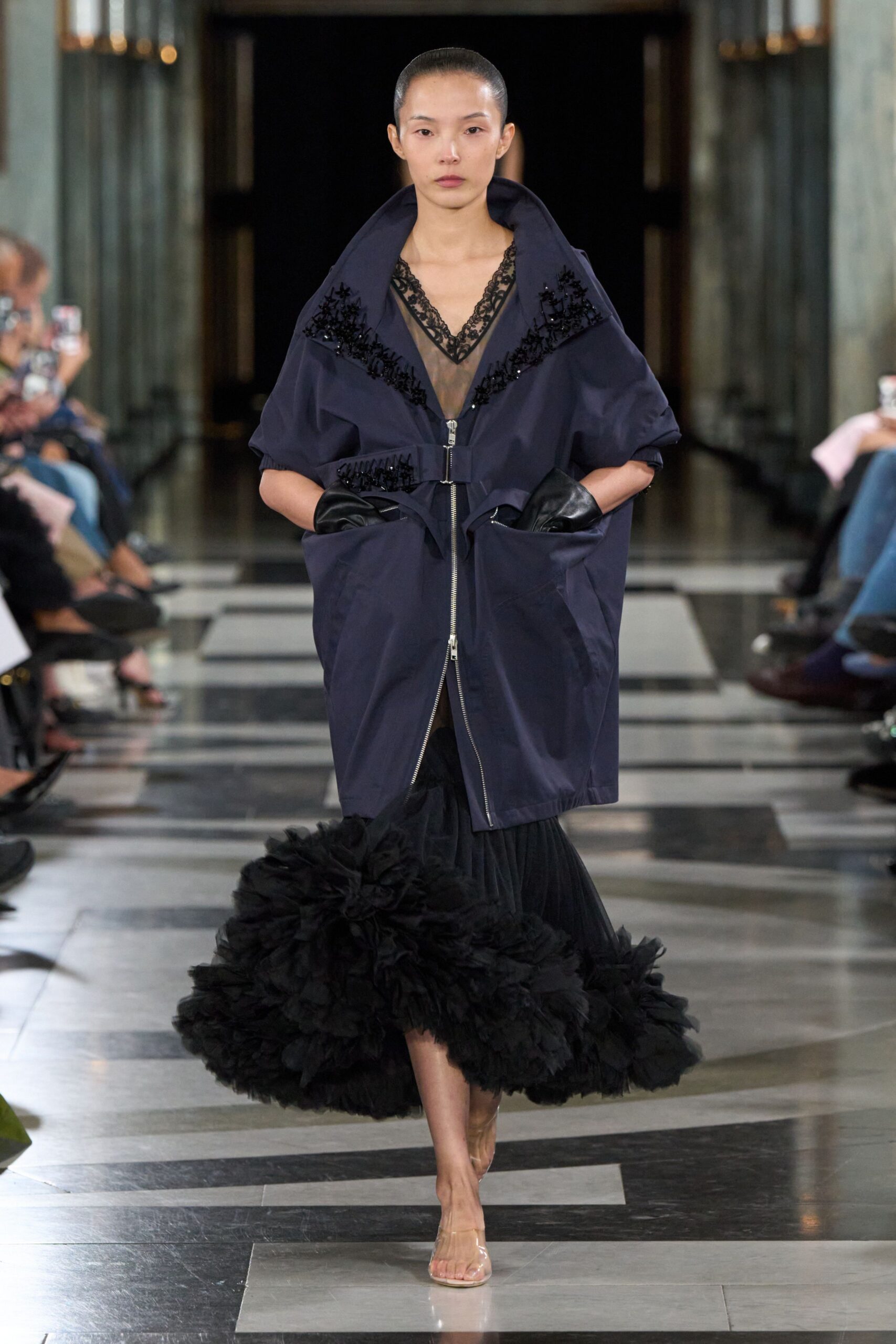 Ink nylon cocoon coat, huge collar beaded with black floral clusters. Sheer black slip dress with scalloped lace V and frothing tulle hem. Black leather gloves tucked into the coat pockets. Clear vinyl sandals, nearly disappearing against the floor. Whatever you wear home when the opera lets out into warm rain.
