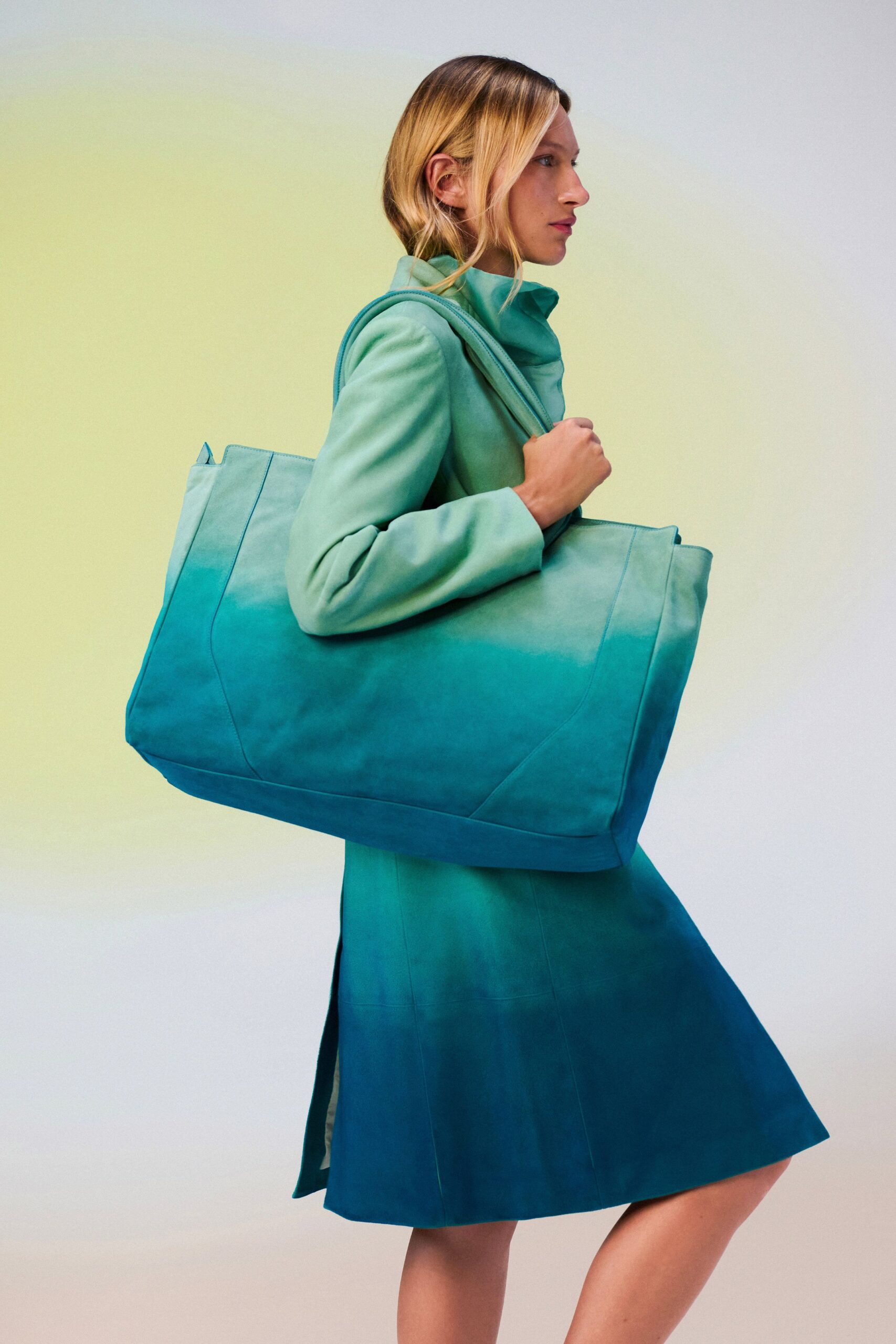 Oversized turquoise suede tote with broad straps and curved paneled seams. Seafoam suede mini dress with a folded funnel neck and side slit. Walking from the marina with salt still drying on your shoulders.