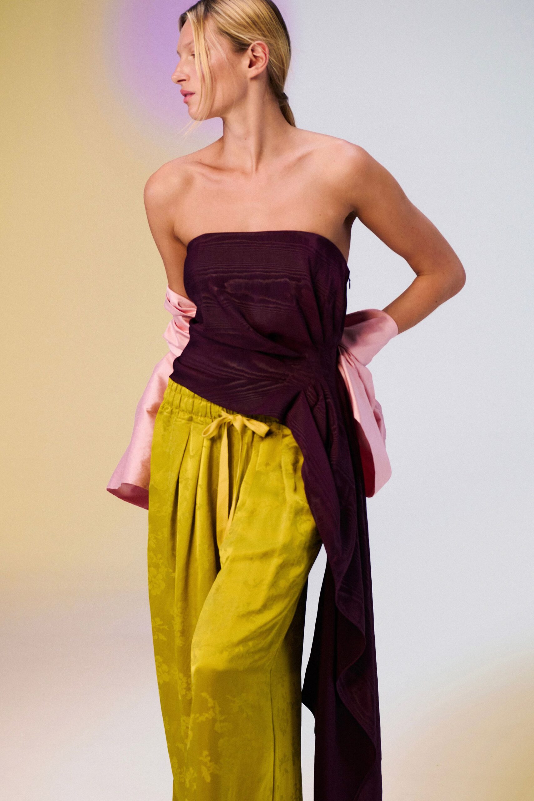 Strapless aubergine wrap top in watered silk, one panel falling nearly to the ankle. Acid-chartreuse jacquard trousers with soft pleats and a tied elastic waist. Blush satin jacket shrugged off the arms. Walking out to the hotel terrace before dessert, sky still holding color.