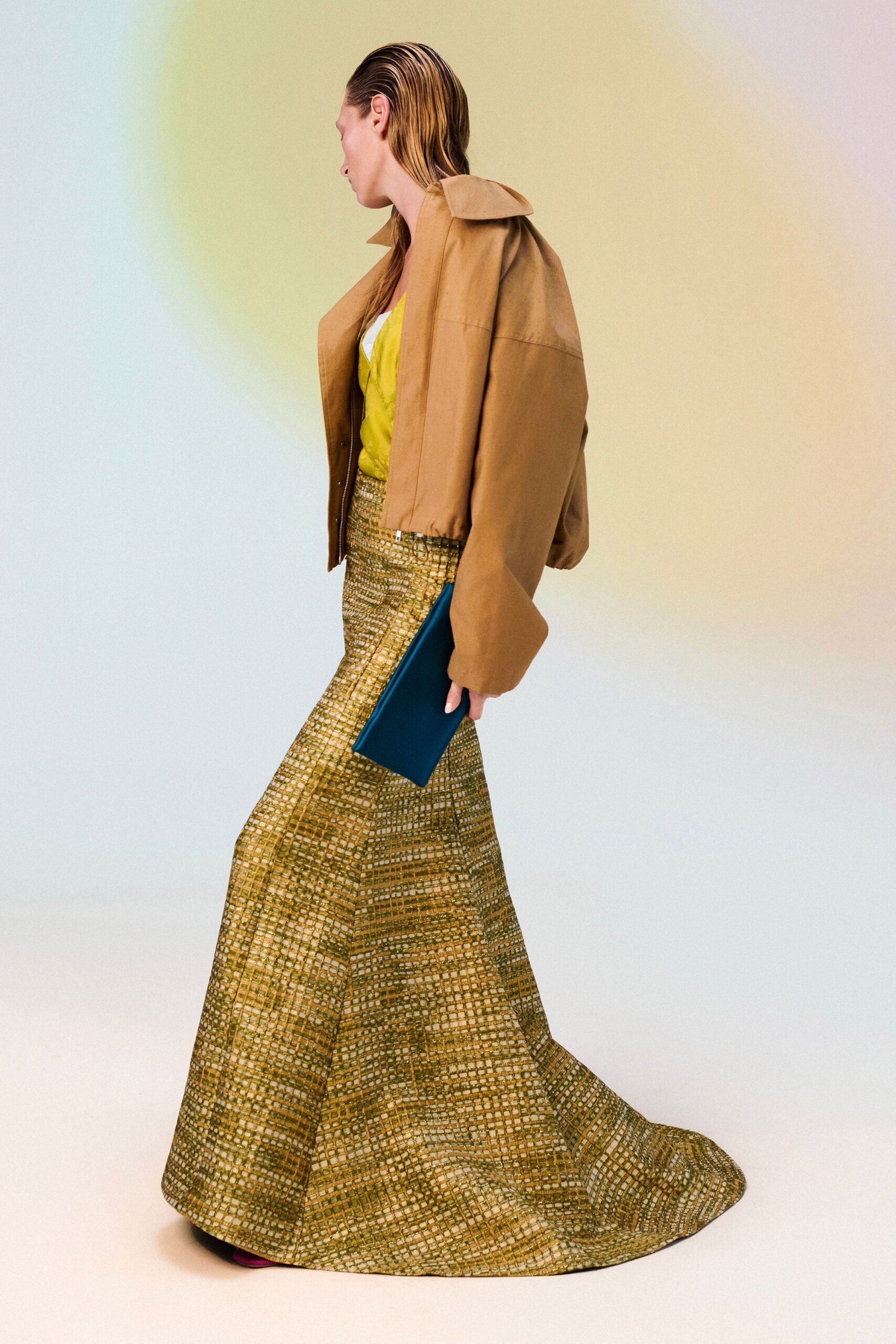 Boxy camel jacket with dropped shoulders and a popped funnel collar. Acid-lime camisole flashing a white inset at the neckline. Floor-length skirt in open grid jacquard, pooling past the heel. Flat teal satin clutch tucked under the arm. Fuchsia toe peeking out. Crossing a hotel atrium at noon with someone else's room key.