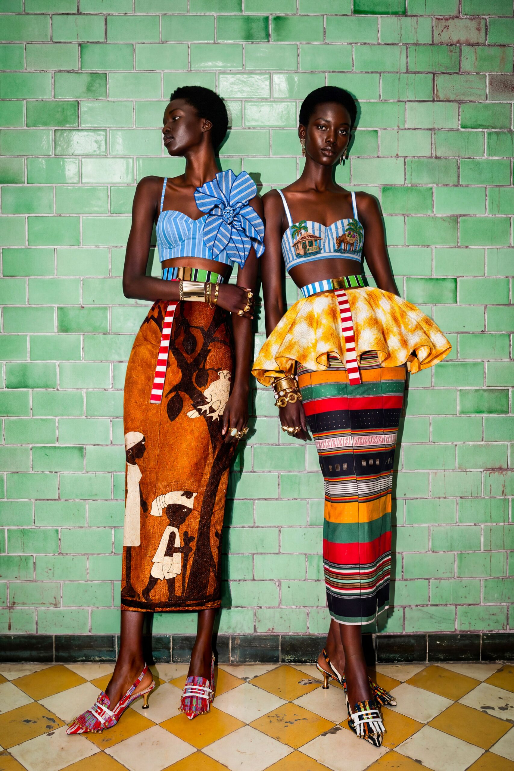 Blue striped bustier with a giant rosette breaking off one strap. Wide waist belt in green, black and cobalt vertical bands. Rust column skirt printed with pale birds and long-limbed figures. Pointed slingbacks in beaded plaid with fringe over the vamp. Waiting for sugarcane juice in a tiled station cafe gone oddly quiet.