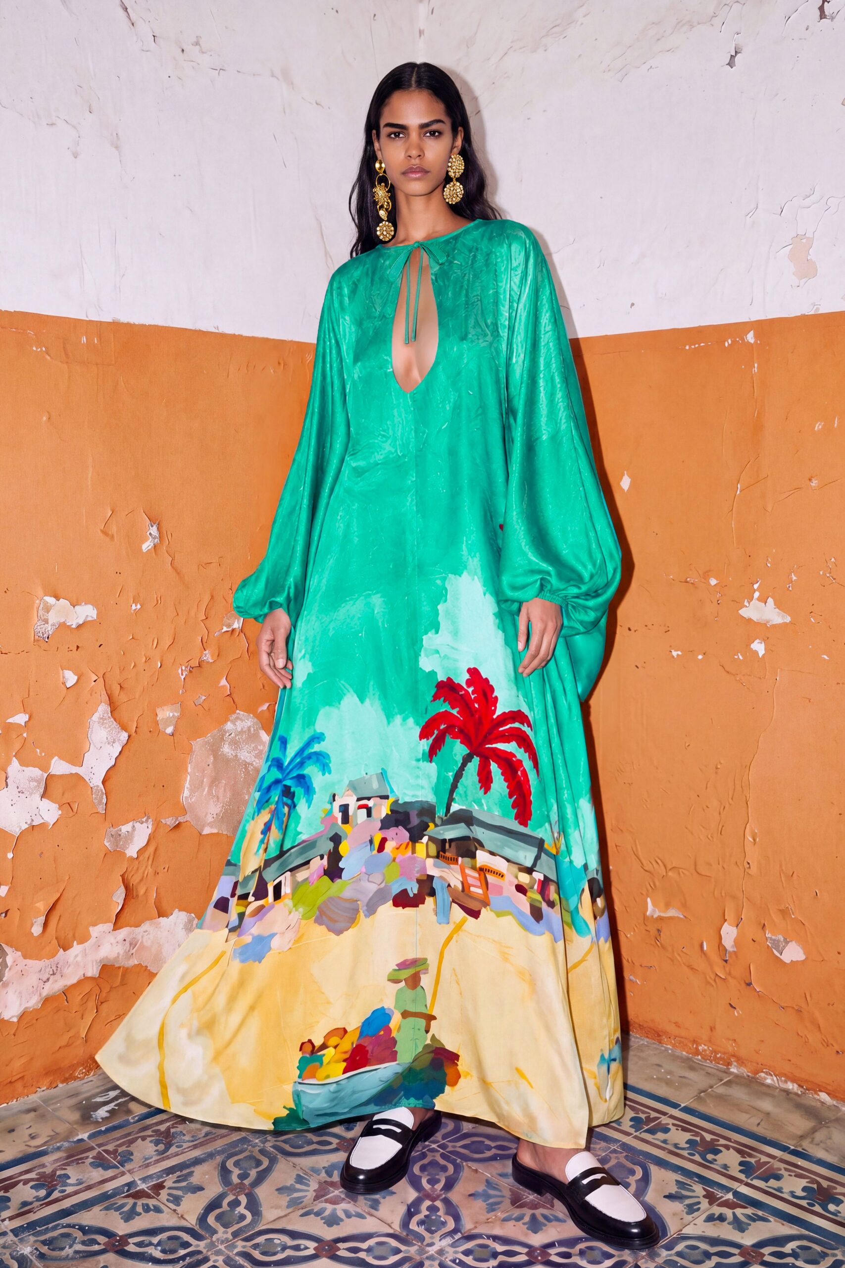 Glossy emerald caftan dress with balloon sleeves and a narrow keyhole tie. Oversized gold cluster drops brushing the jaw. Black-and-white leather loafers worn backless like slippers. Salt air on cracked tiles, stopping for lunch above a painted fishing cove.