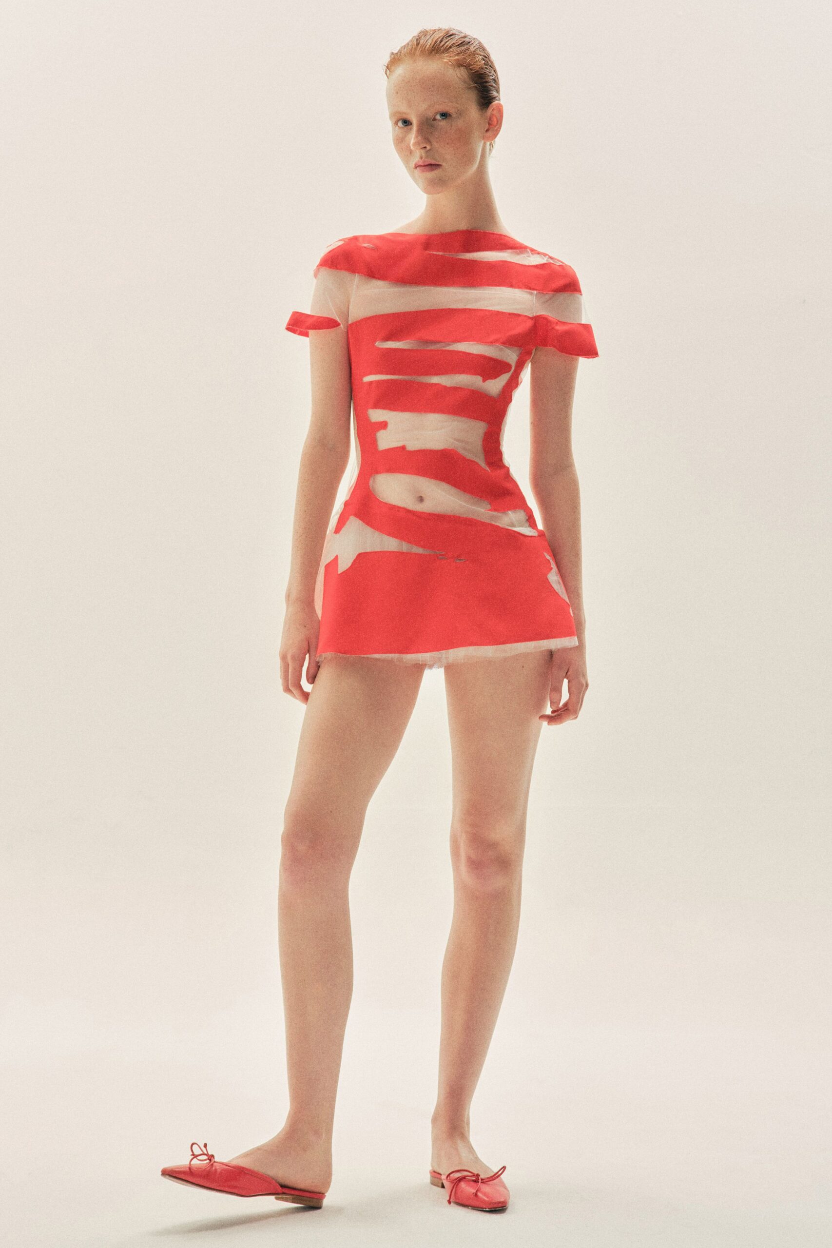 Sheer nude mesh mini dress slashed with coral bands and a frayed hem. Flat coral leather mules with loose bow ties at the square toe. For crossing sunburnt paving after a swim, still half wrapped in a towel.