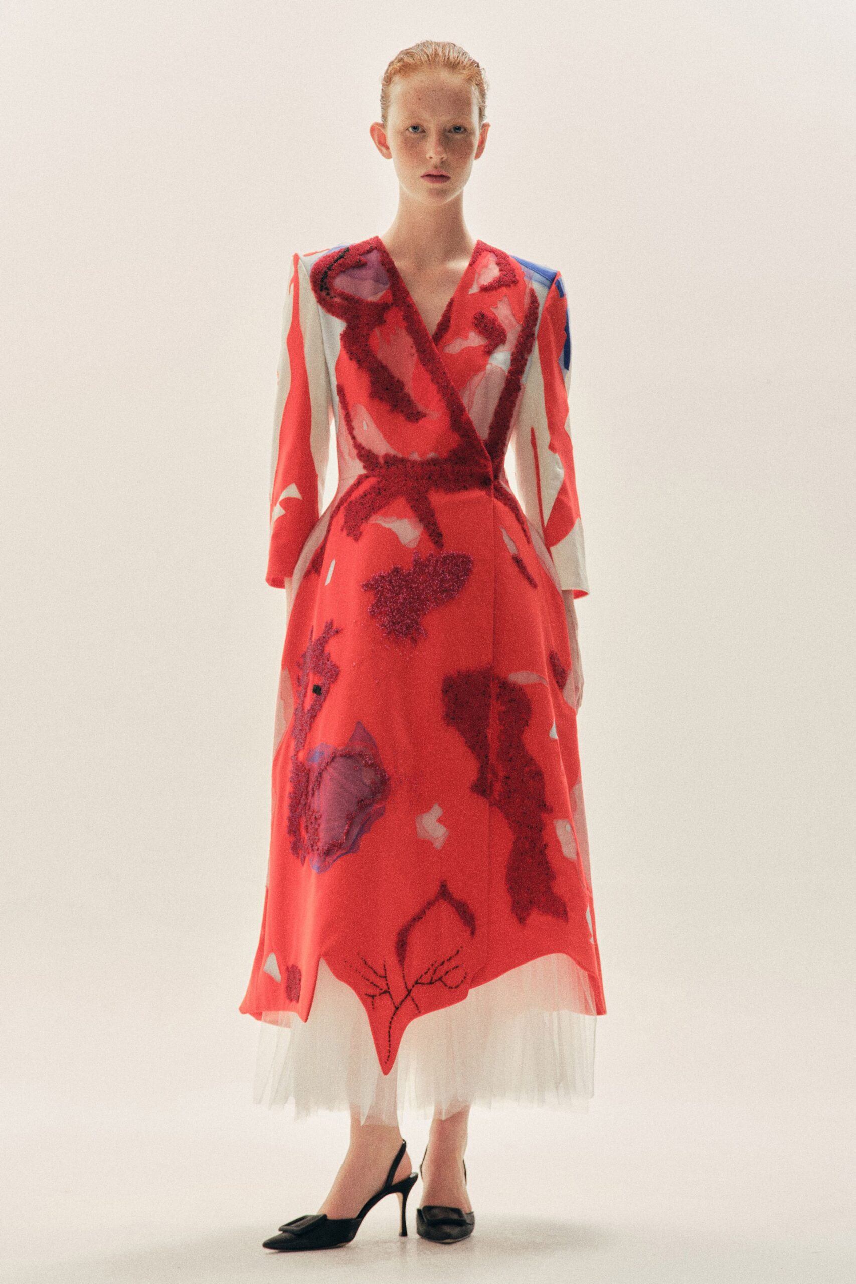 Scarlet wrap dress with fuzzy burgundy appliques and a pointed handkerchief hem. White tulle underskirt fogging out below the calf-length dress. Black slingback pumps with square buckles at the pointed toe. Museum atrium at noon, still carrying petals from the opening.