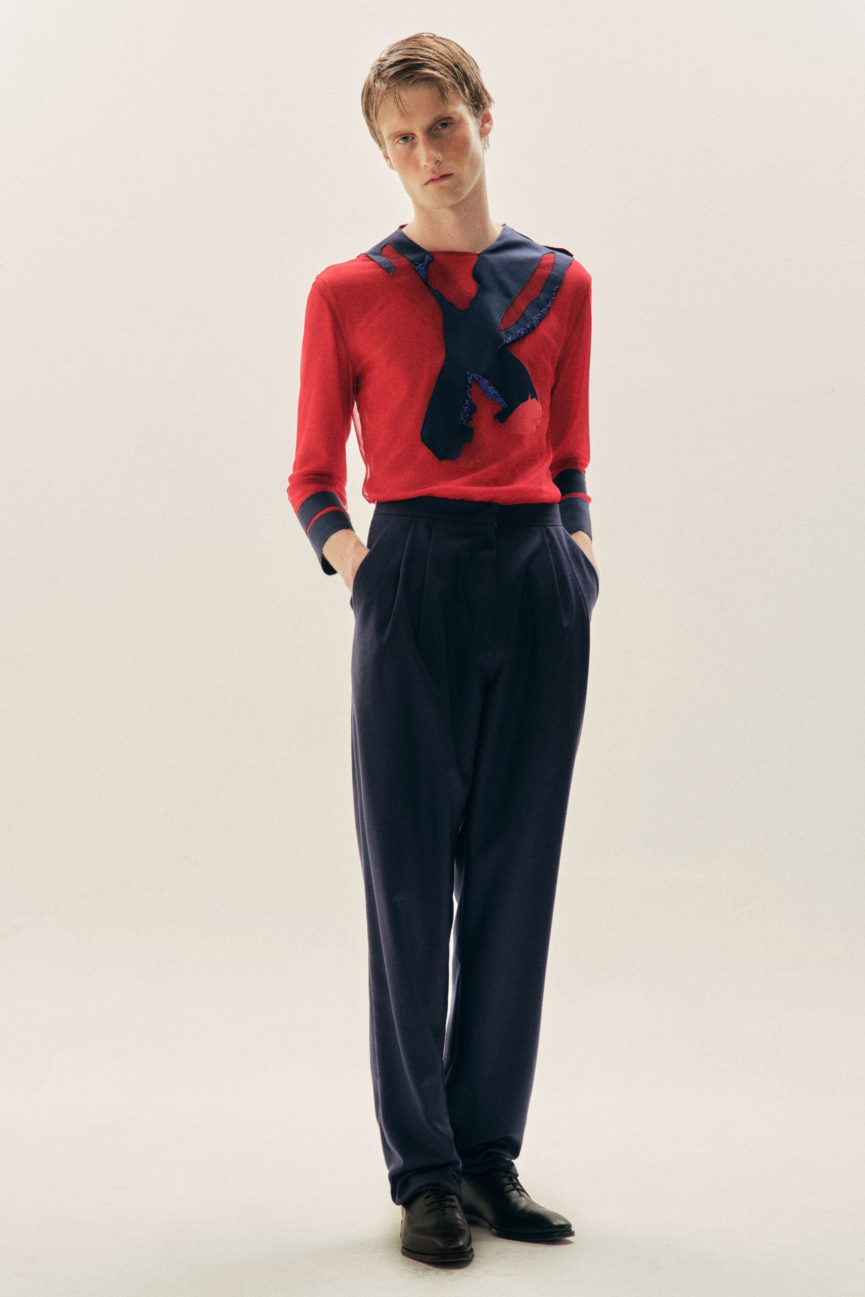 Red fine-gauge knit top with navy appliques edged in cobalt sequins. Ink pleated trousers, cut full through the leg. Black leather derbies. Walking into a recital hall before the ushers have opened every door.