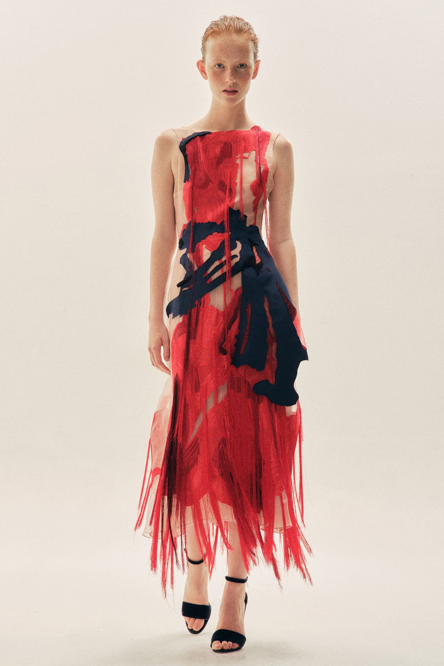 Sheer nude slip dress veiled in scarlet gauze shreds and inky applique swathes. Black ankle-strap sandals with wide velvet toe bands. Whatever you wear to read the last note before burning it.