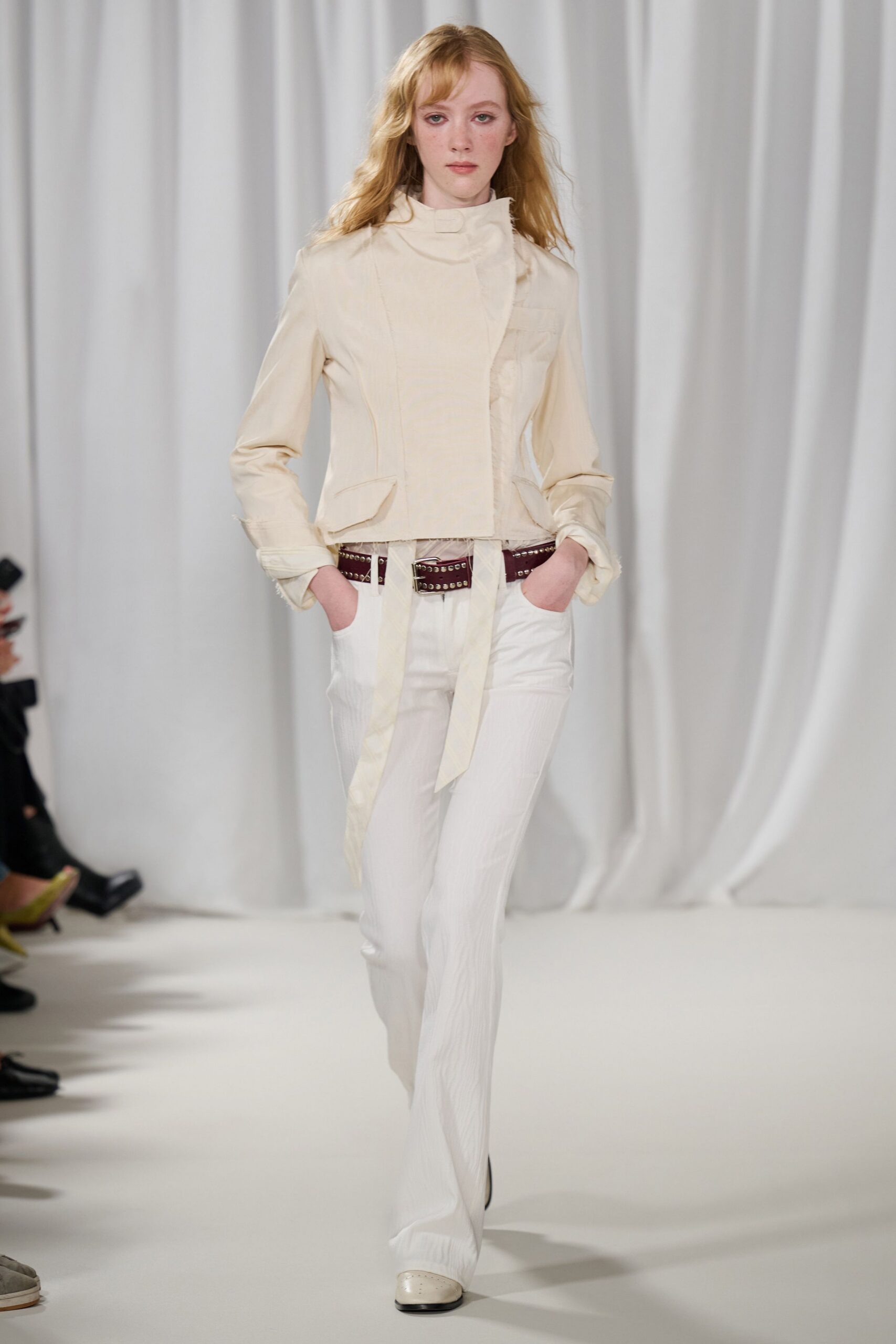 Cream fitted jacket with a high stand collar and frayed cuffs. Oxblood leather belt punched with two rows of silver studs. White straight trousers in a faintly crinkled stripe. Square-toe cream shoes with tiny perforations at the vamp. For the drive back from a courthouse wedding, flowers sliding on the back seat.