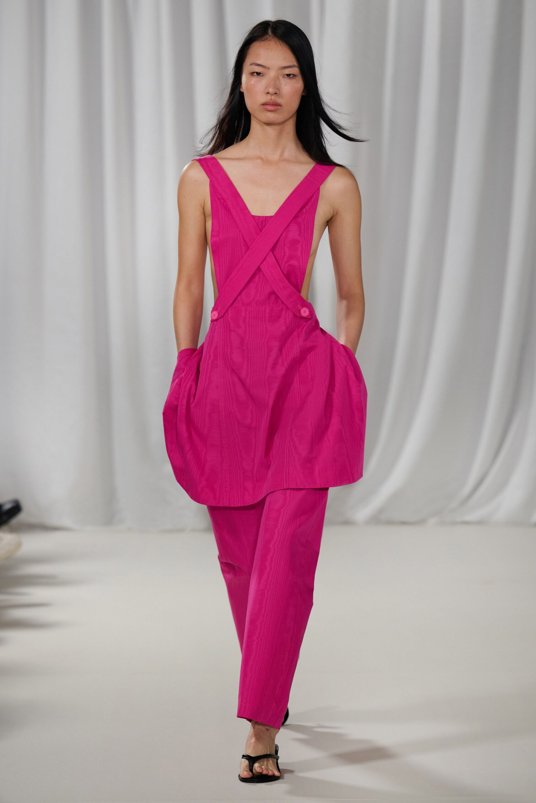 Fuchsia moire tunic with crossed straps and rounded pocketed hips. Matching slim trousers in the same watered silk effect. Black thong sandals, barely-there sole. Walking into a wedding lunch before anyone has found the shade.