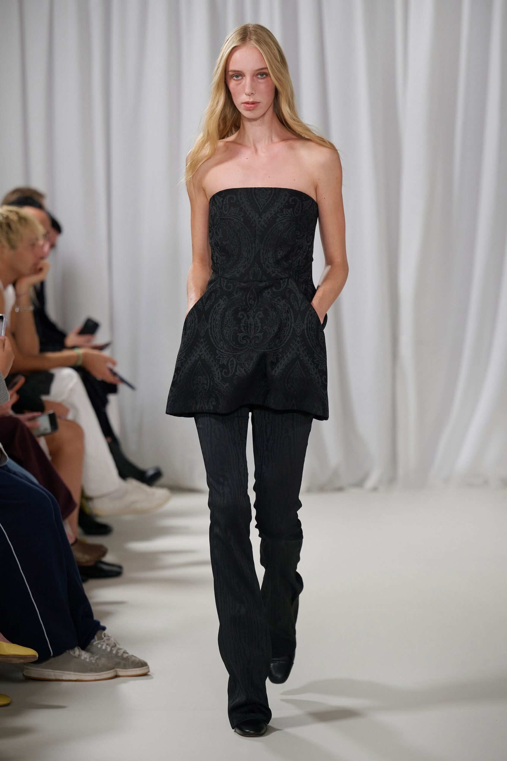 Black damask jacquard tunic, cut straight across the chest with pocketed hips. Slim black trousers in a tonal moire-like stripe, breaking softly over the shoe. Square-toe black shoes. For arriving early to a wedding and drifting out to the gravel drive.