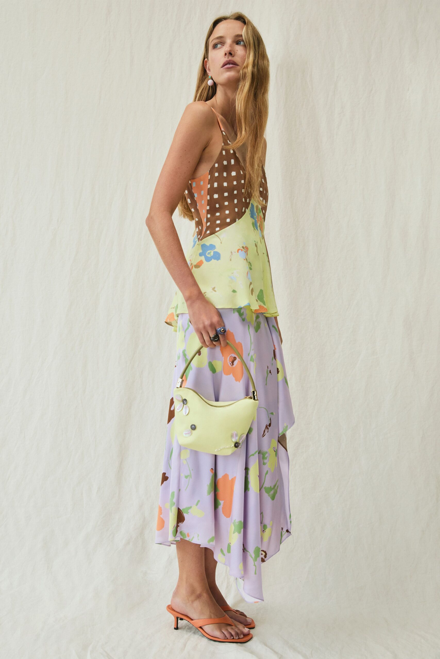 Chocolate slip camisole spliced with peach panels and white painted dots. Lilac floral midi skirt falling in an uneven handkerchief hem. Butter-yellow crescent bag dotted with tiny flower appliques. Apricot thong mules on a low spool heel. Walking back from a garden lunch with nectar on your wrist.