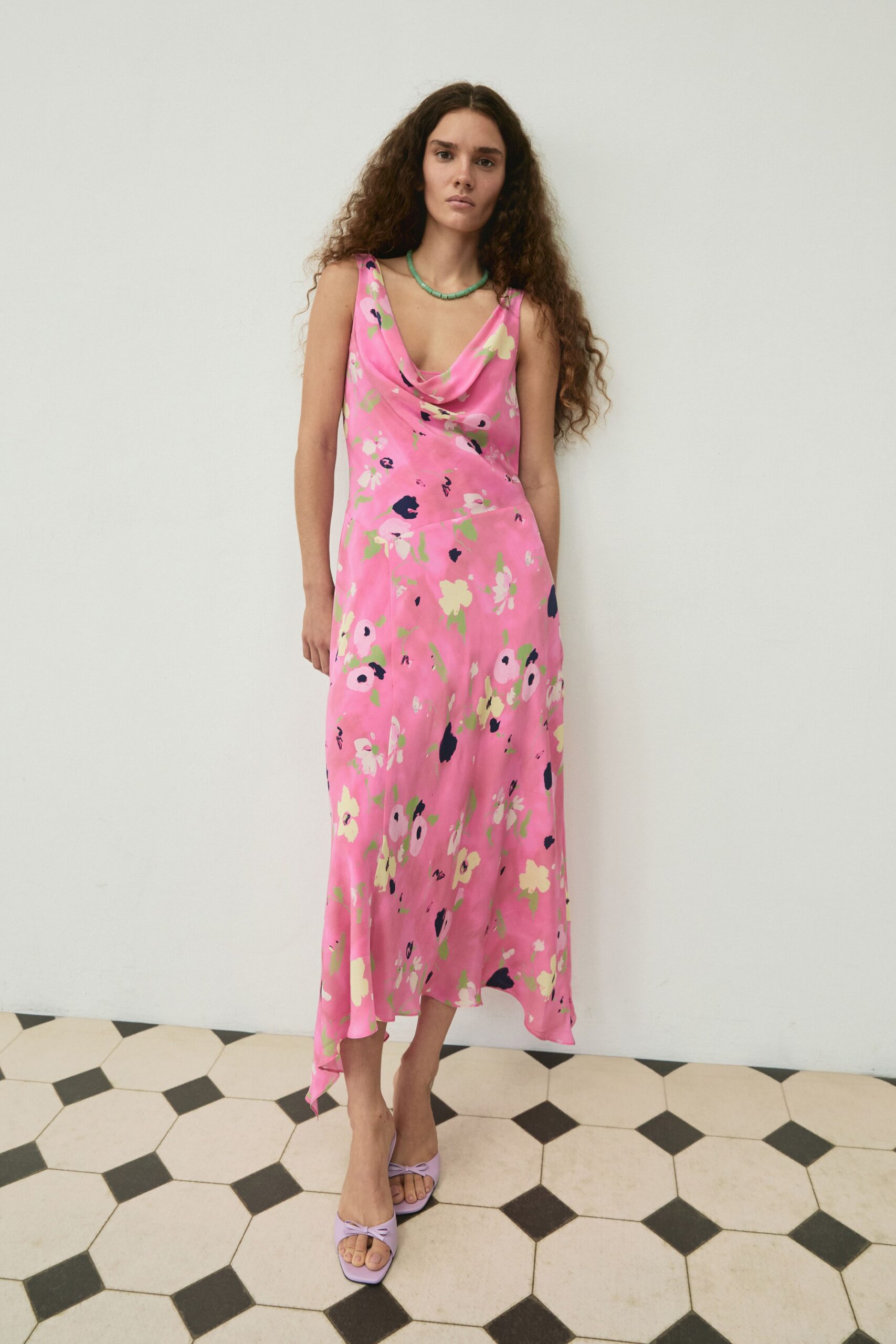 Turquoise bead necklace, short and close to the collarbone. Pink satin slip dress with a cowl neck and scattered cream blossoms. Lilac square-toe mules topped with a small twisted bow. Breakfast on a tiled veranda before the heat settles in.