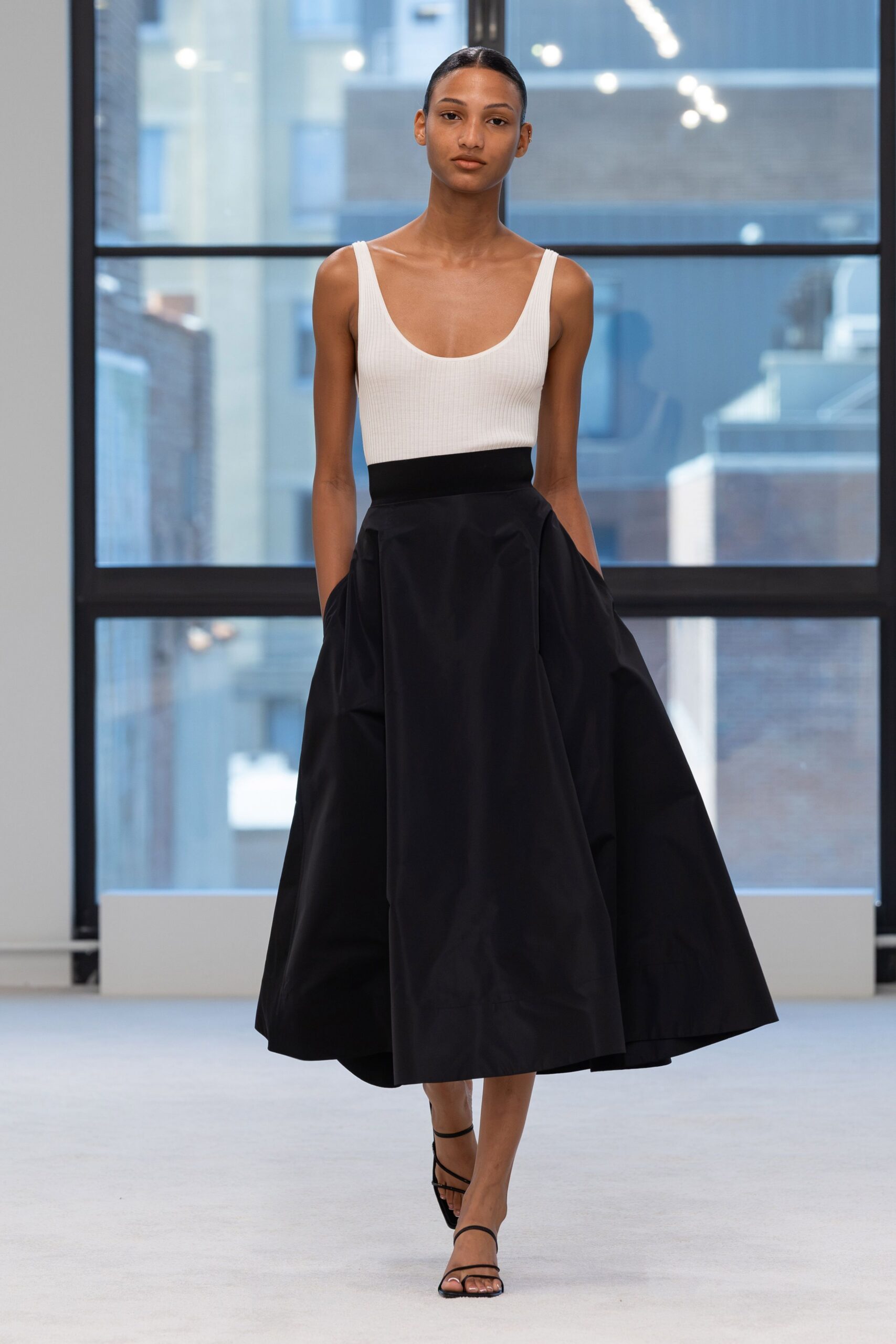 White ribbed knit bodysuit with a deep scooped neckline. Black taffeta midi skirt, densely gathered into a wide waistband. Bare black ankle-strap sandals. Crossing a museum atrium before the string quartet starts.