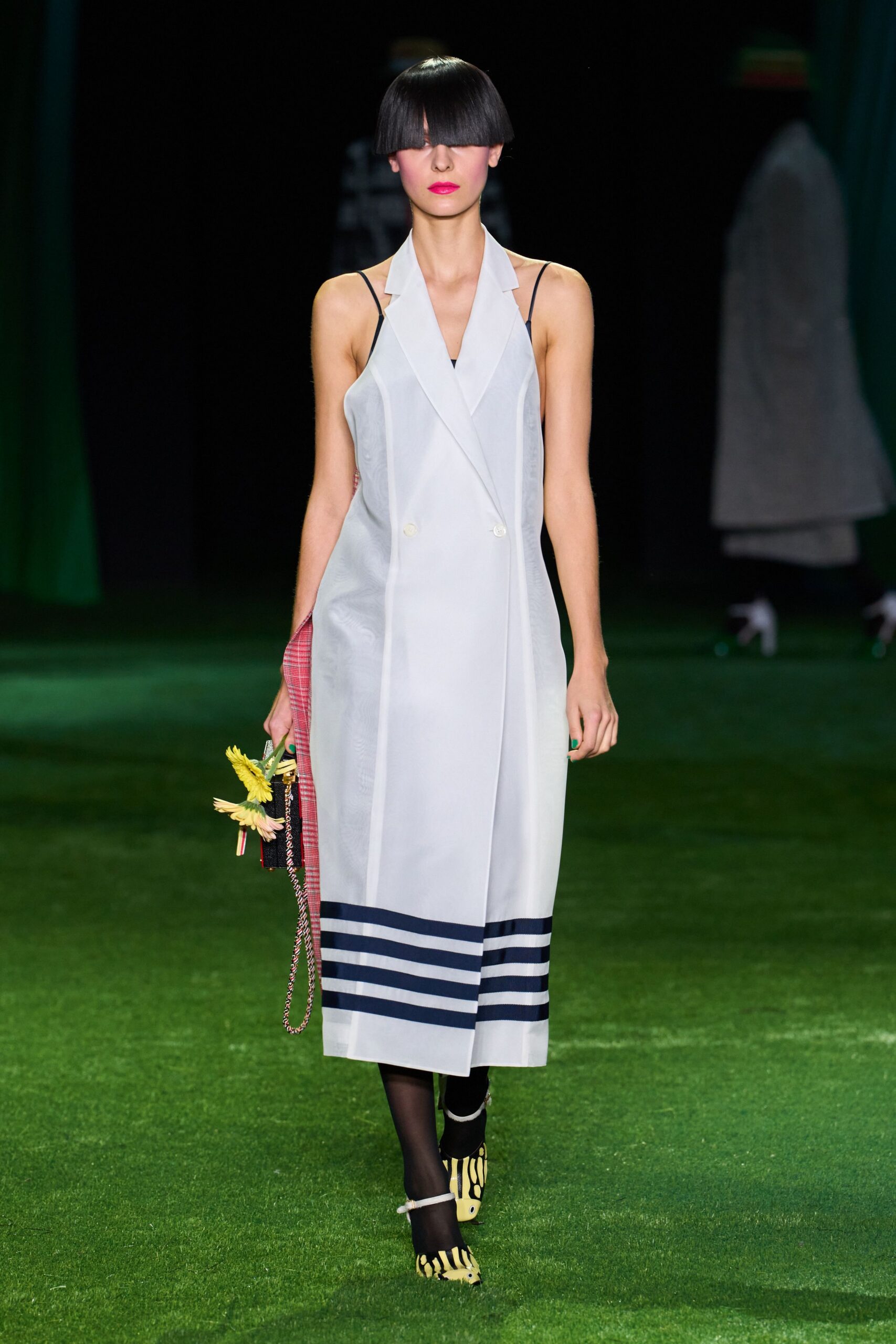 Sheer pale grey wrap dress with lapels and navy bands at the hem. Black camisole slip traced by thin straps under the organza. Black sheer stockings. Yellow-and-black striped pumps with white ankle straps. Plaid clutch dangling chain and a bunch of yellow daisies. Crossing a lawn after the garden party has thinned out.