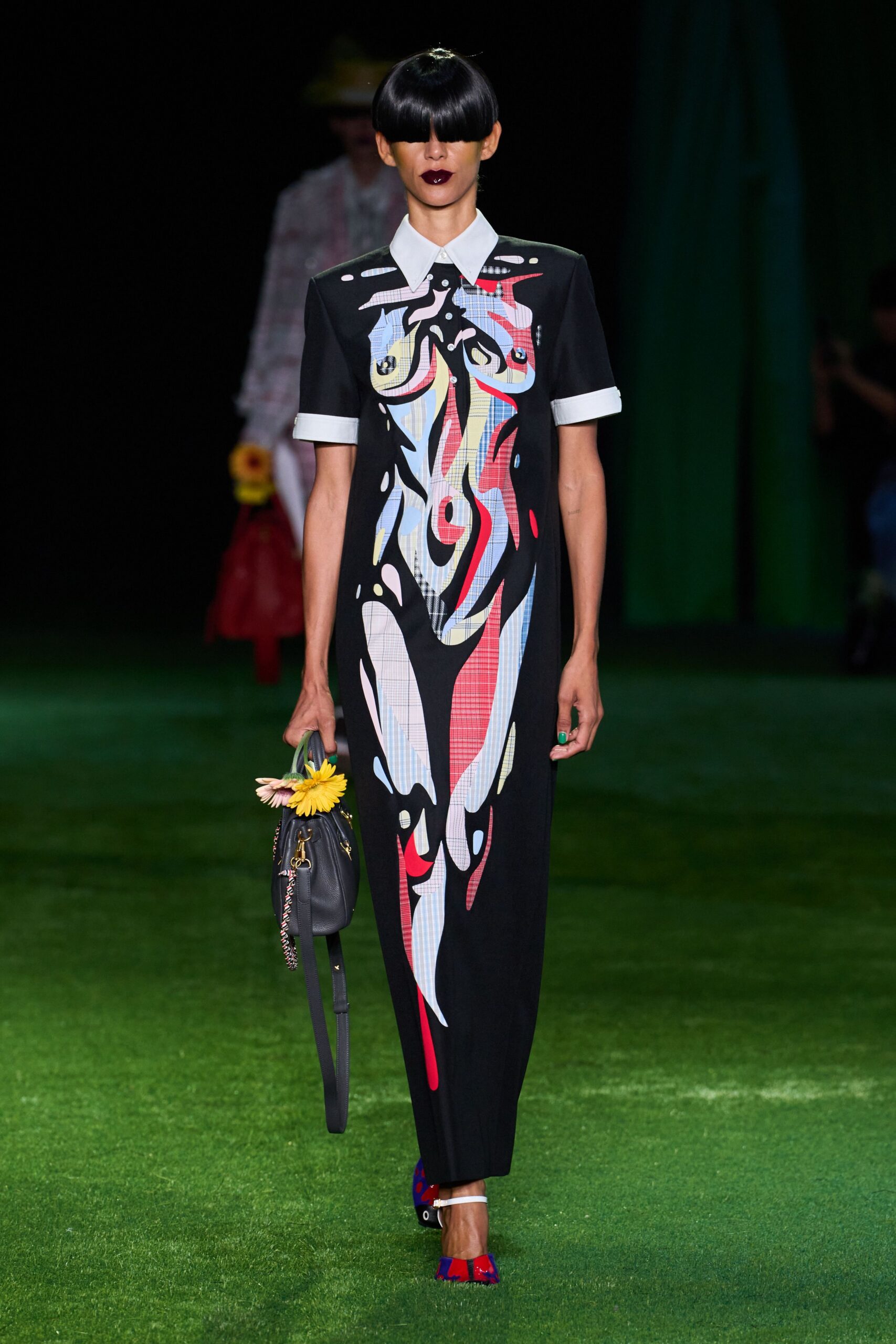 Black shirt dress with pale cuffs and collar, overlaid by a face in spliced checks. Slate leather satchel with a daisy tucked into the handle. Blue-and-red pumps with a white ankle strap. Crossing a golf green after the wedding, still carrying the table flowers.