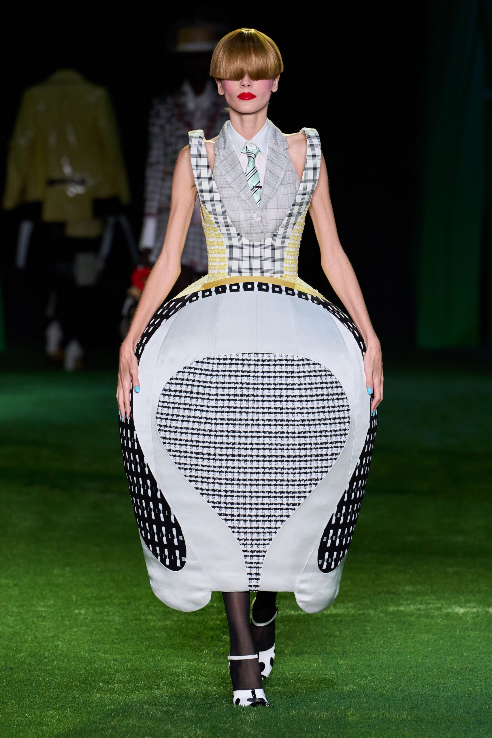White pointed-collar shirt under a pale mint striped tie. Plaid bodice and vast panniered skirt, edged with yellow boucle and graphic cutouts. Sheer black tights. White pumps with black spots and a slim strap. Crossing a croquet lawn after someone turned the dress code into a dare.