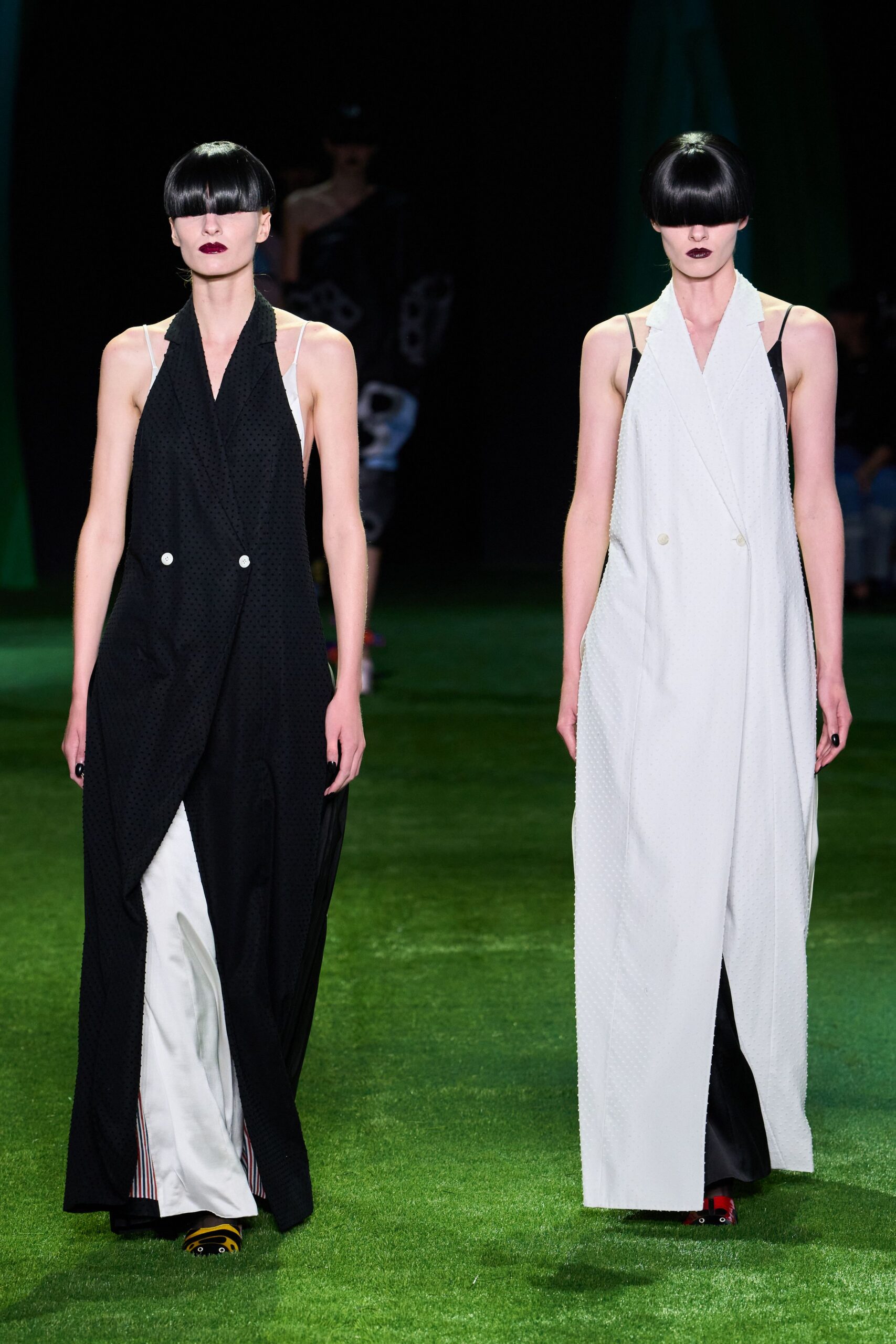 White double-breasted coat dress in dotted jacquard, cut open below the buttons. Black satin slip peeking through the front slit and side armholes. Red sandals with a black strap. Crossing a lawn after midnight when the wedding has thinned out.