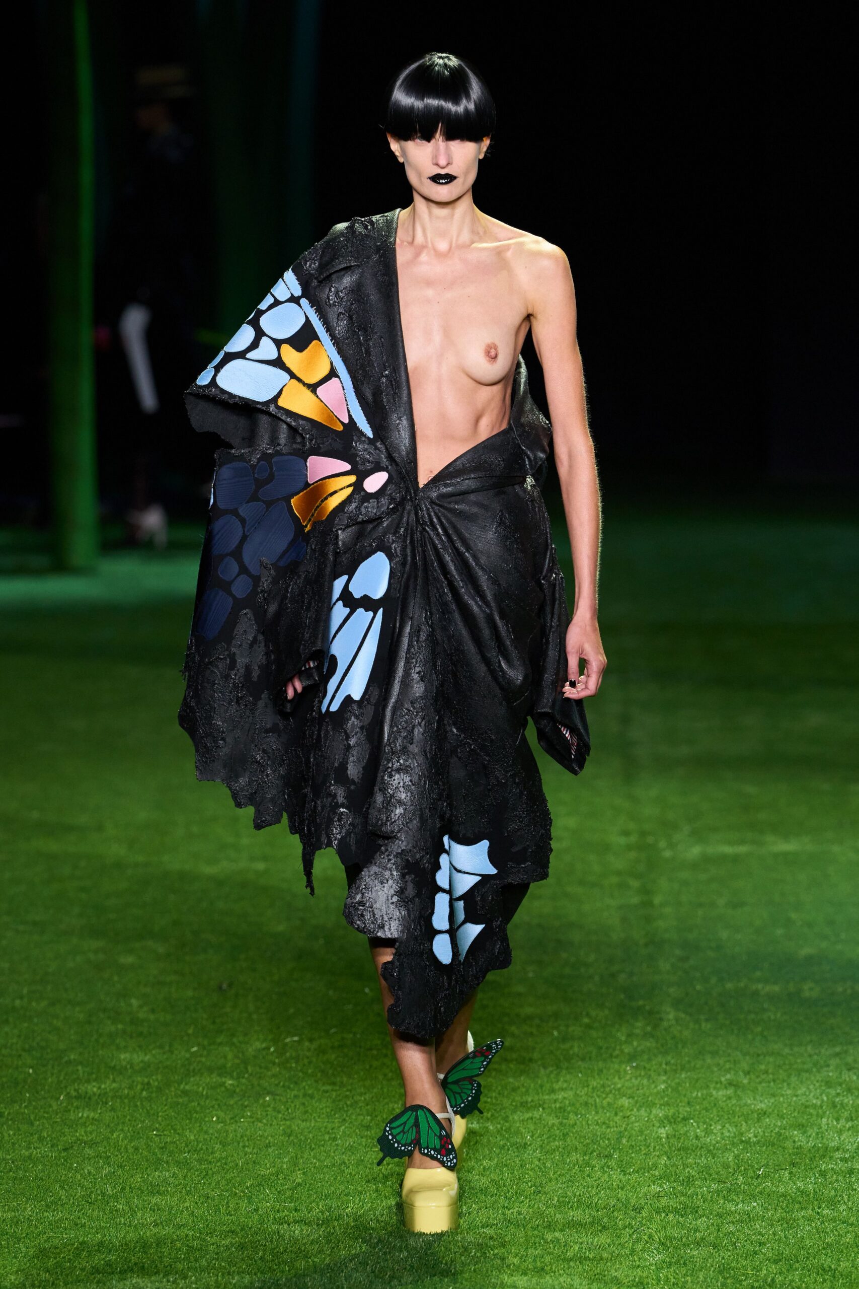 Asymmetric black devore dress, knotted at the waist with butterfly-wing panels. Butterfly appliques hovering over pale yellow patent platforms. Crossing a public greenhouse after dark, damp soil still warm underfoot.