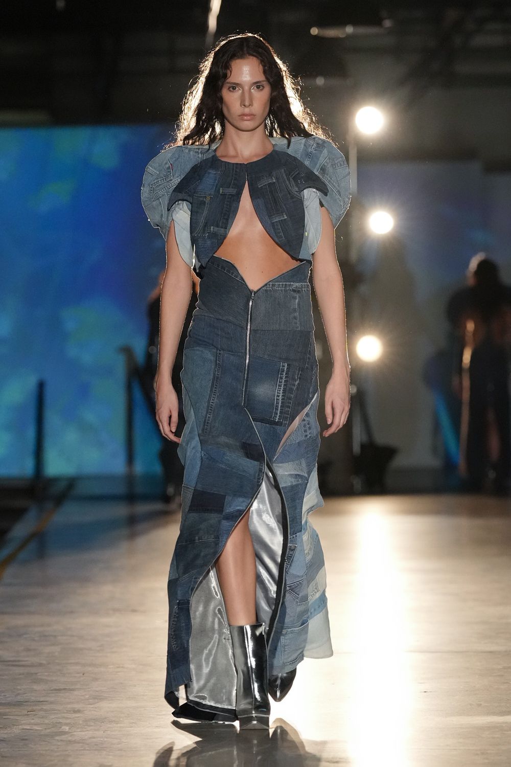 Patchworked denim bolero with puffed pale panels and raw-edged tabs. Strapless denim patchwork column, split by a long off-center zip. Mirror-shine silver boots with a sharp pointed toe. Crossing an empty gym floor after the dance got moved indoors.
