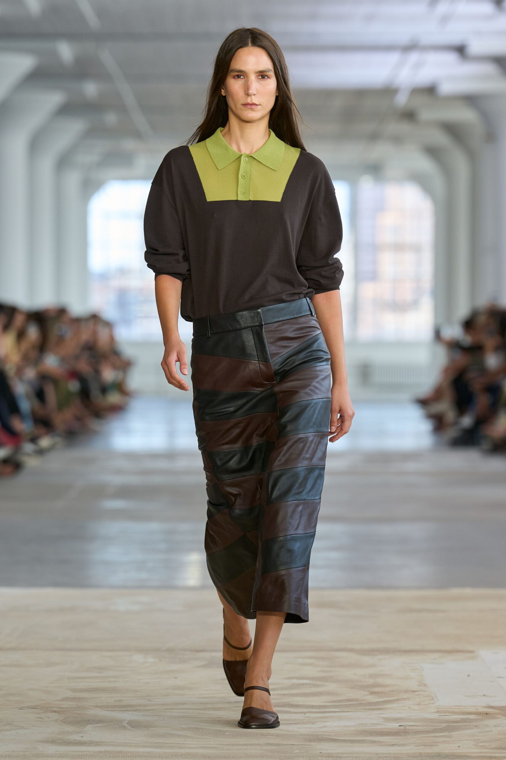 Dark brown fine-knit polo with a chartreuse bib and three-button placket. Middy skirt pieced from wide oxblood and black leather bands. Brown square-toe slingback flats with a narrow instep strap. Walking back from lunch through an office tower still humming on generator power.