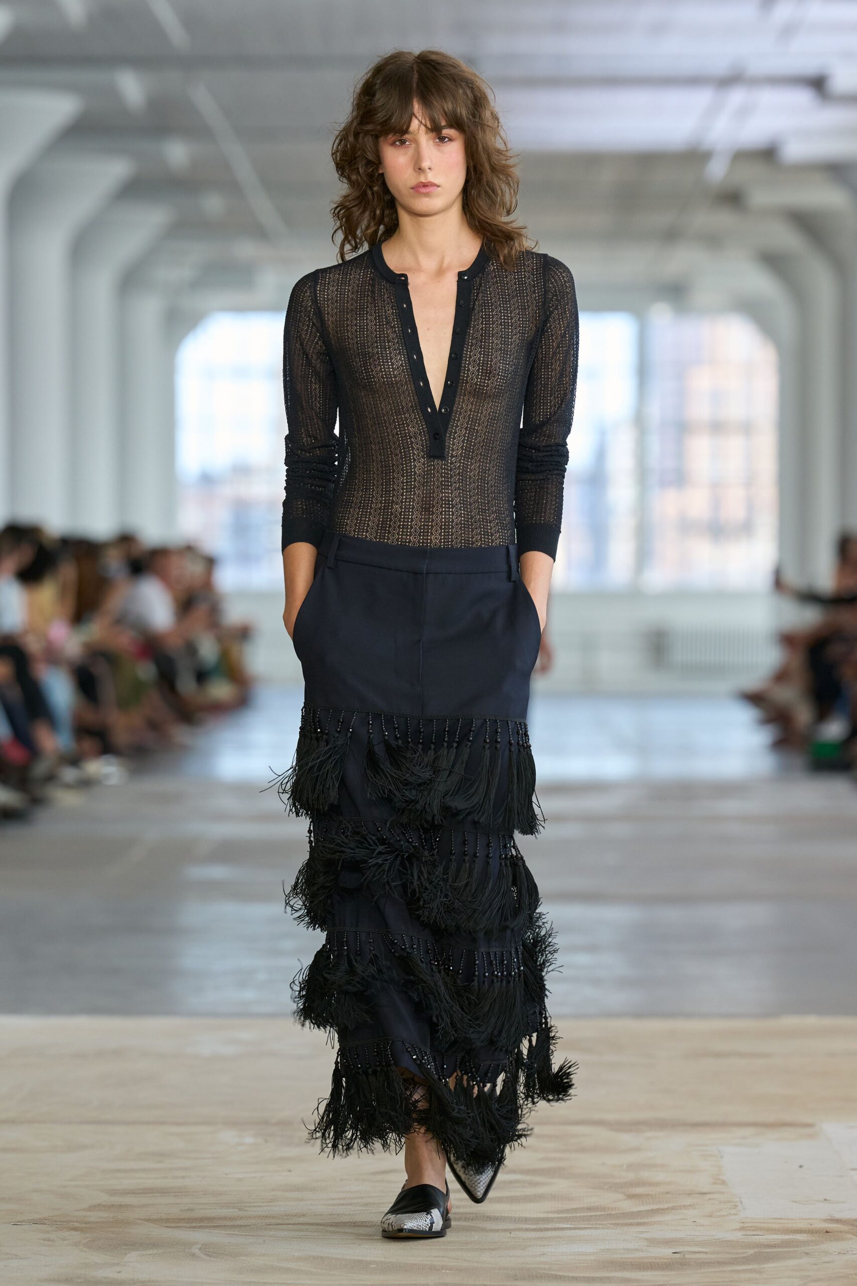 Sheer black pointelle knit top with a plunging snap placket. Low-slung black skirt dropping into tiered fringe bands threaded with jet beads. Black pointed flats with metallic snakeskin at the toe. Walking the long hall after a wedding, confetti still stuck to your cuff.