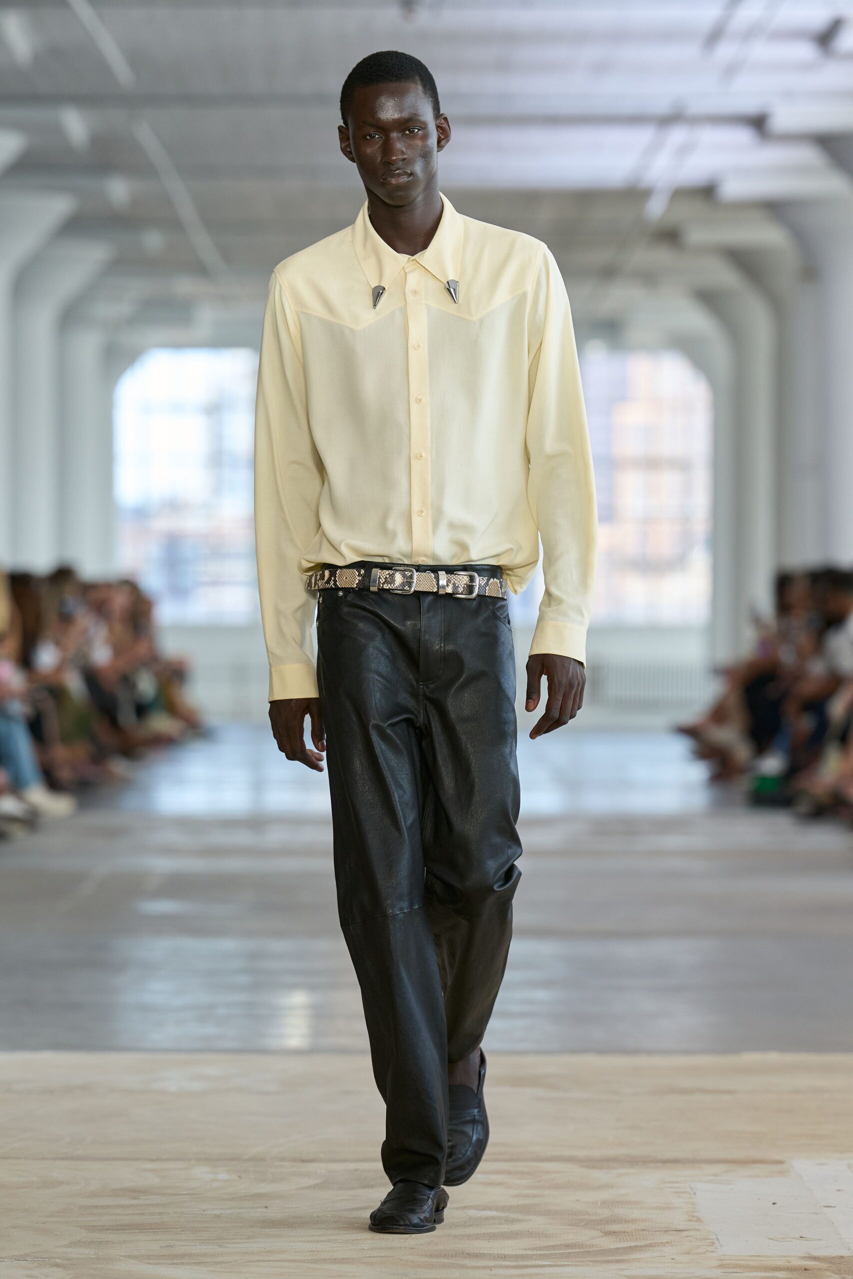 Buttercream shirt with a sheer yoke and pointed metal collar tips. Python belt fastened with twin square buckles. Black leather trousers falling straight with a soft crease at the knee. Black square-toe shoes. Office tower Sunday, nobody else on the floor but the cleaners.