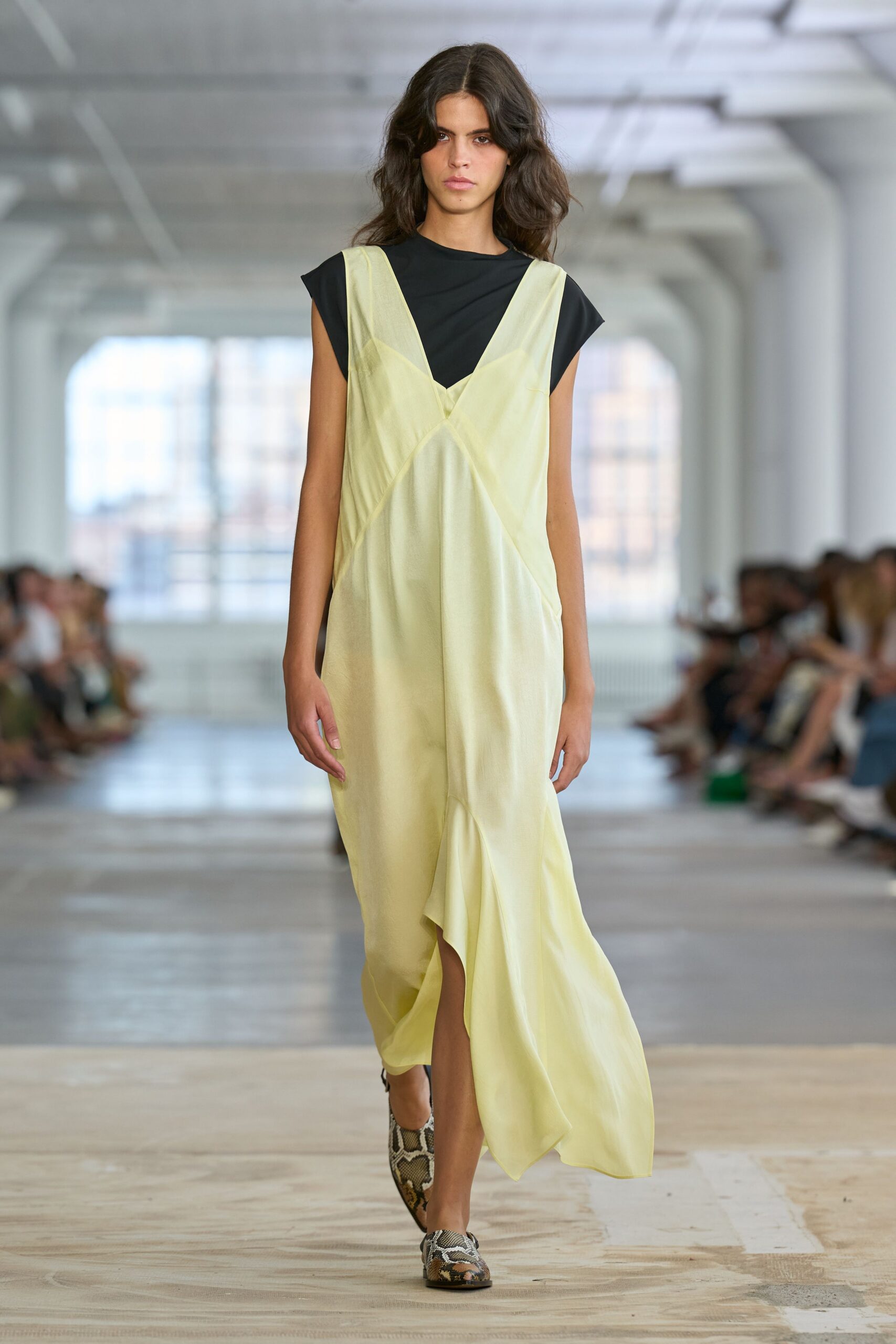 Black jersey tee with cut-on cap sleeves and a close crewneck. Pale citron satin slip dress, seamed diagonally into a long twisted front slit. Python-print pointed flats. Crossing a hotel lobby at breakfast with yesterday's room key still working.