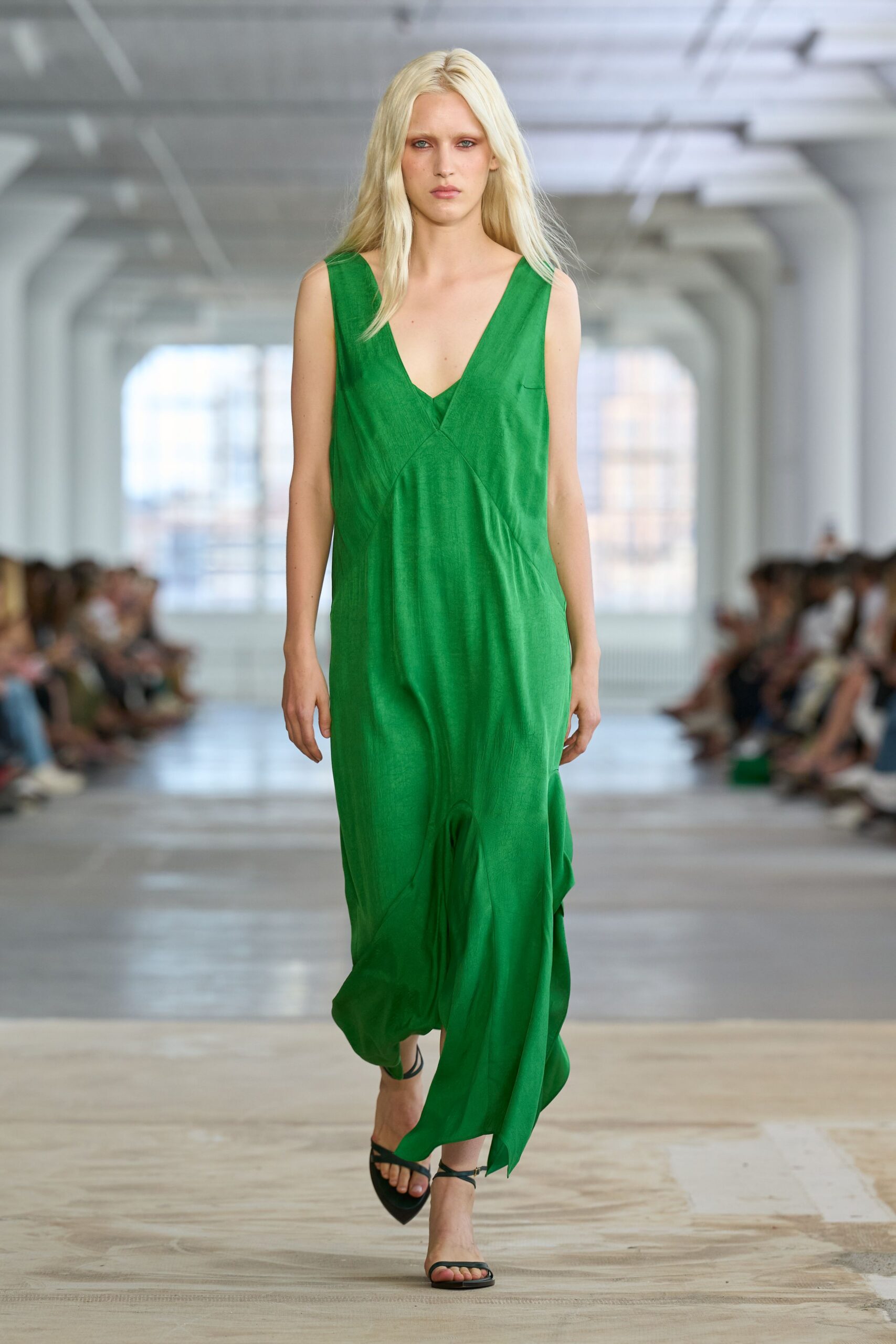 Emerald sleeveless slip dress in washed silk, deep V and curved seam joins. Black thong sandals with fine wraparound straps at the ankle. Crossing a hotel courtyard just after the pool has closed.
